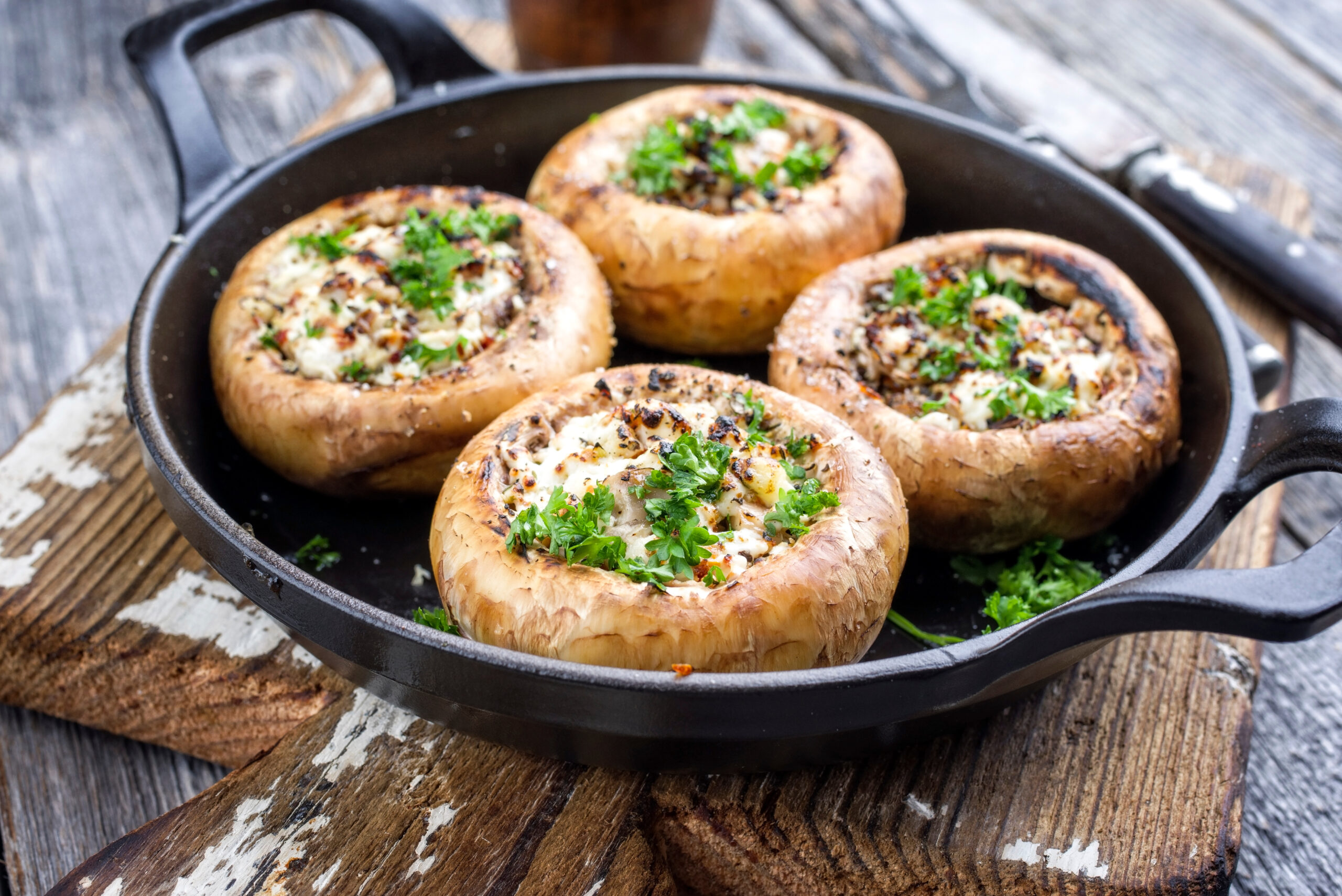 Stuffed mushrooms with cheese and herbs in a cast-iron skillet on a rustic wooden table, garnished with parsley.