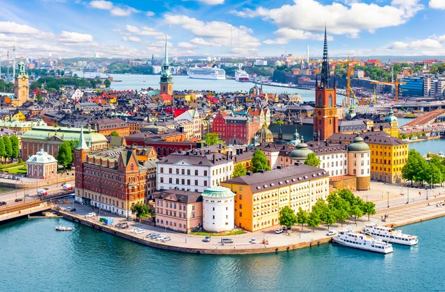 Aerial view of Stockholm's Gamla Stan area with colorful historic buildings along the harbor and boats on the water under a blue sky.