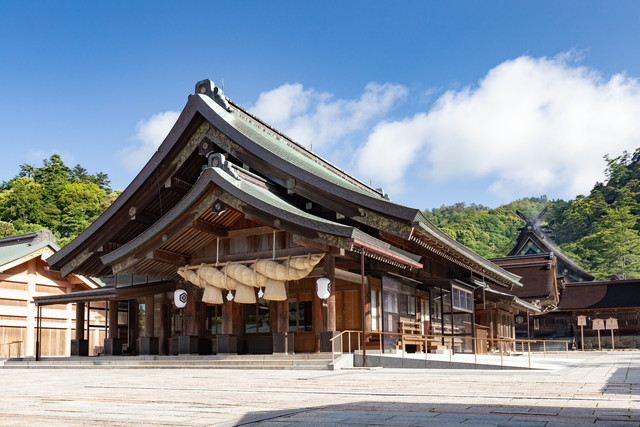 Shinto shrine building with wooden architecture, large straw rope (shimenawa) and paper lanterns on a sunny day