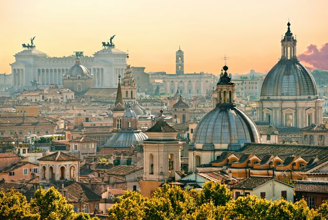 Rome cityscape at sunset with domed churches and terracotta rooftops forming a warm horizon.