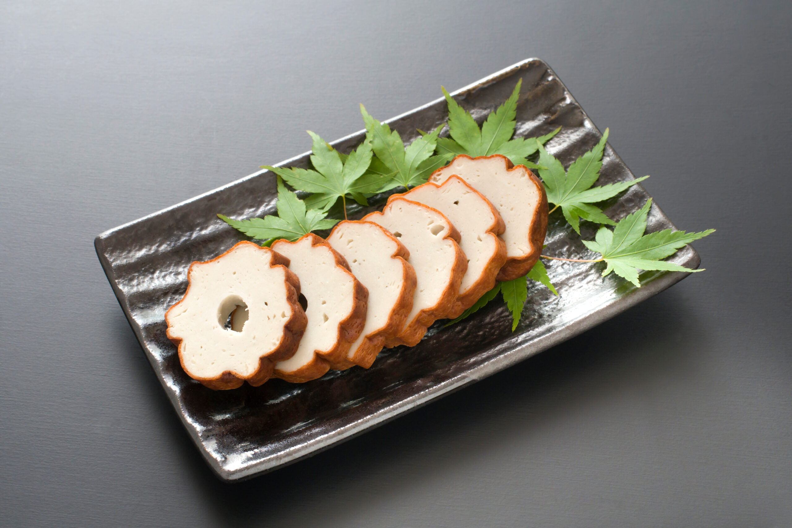 Sliced white bread fanned on a dark rectangular plate, garnished with green maple leaves.