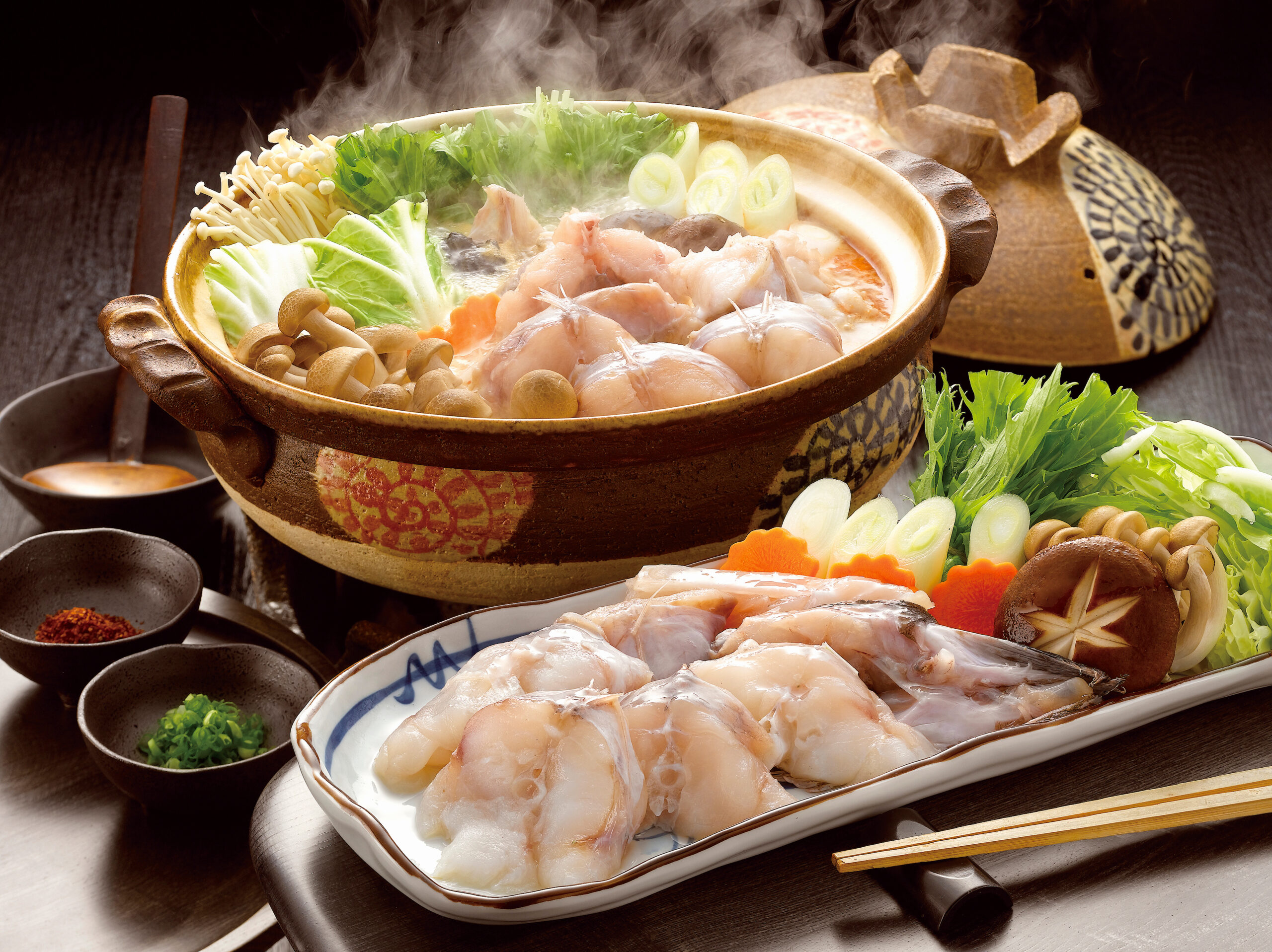 Hot pot filled with raw chicken, leafy greens, mushrooms, leek slices, and vegetables steaming in a ceramic pot.