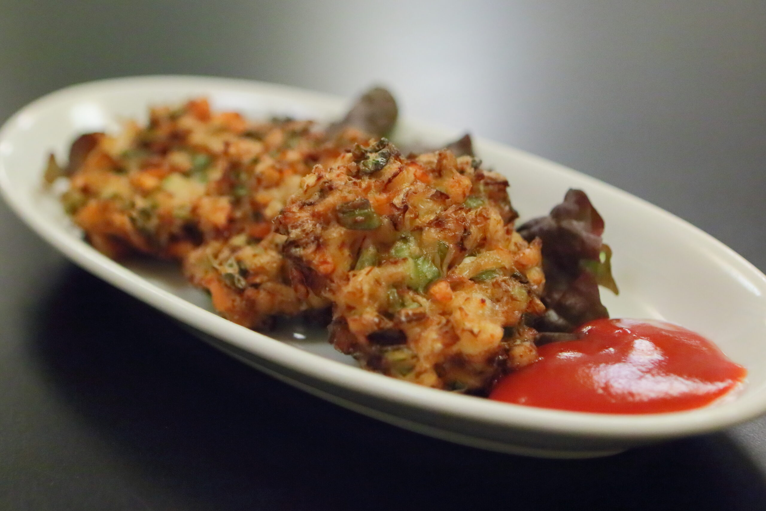 Two vegetable-filled croquettes on a white plate with a red sauce on the side, close up of the dish.