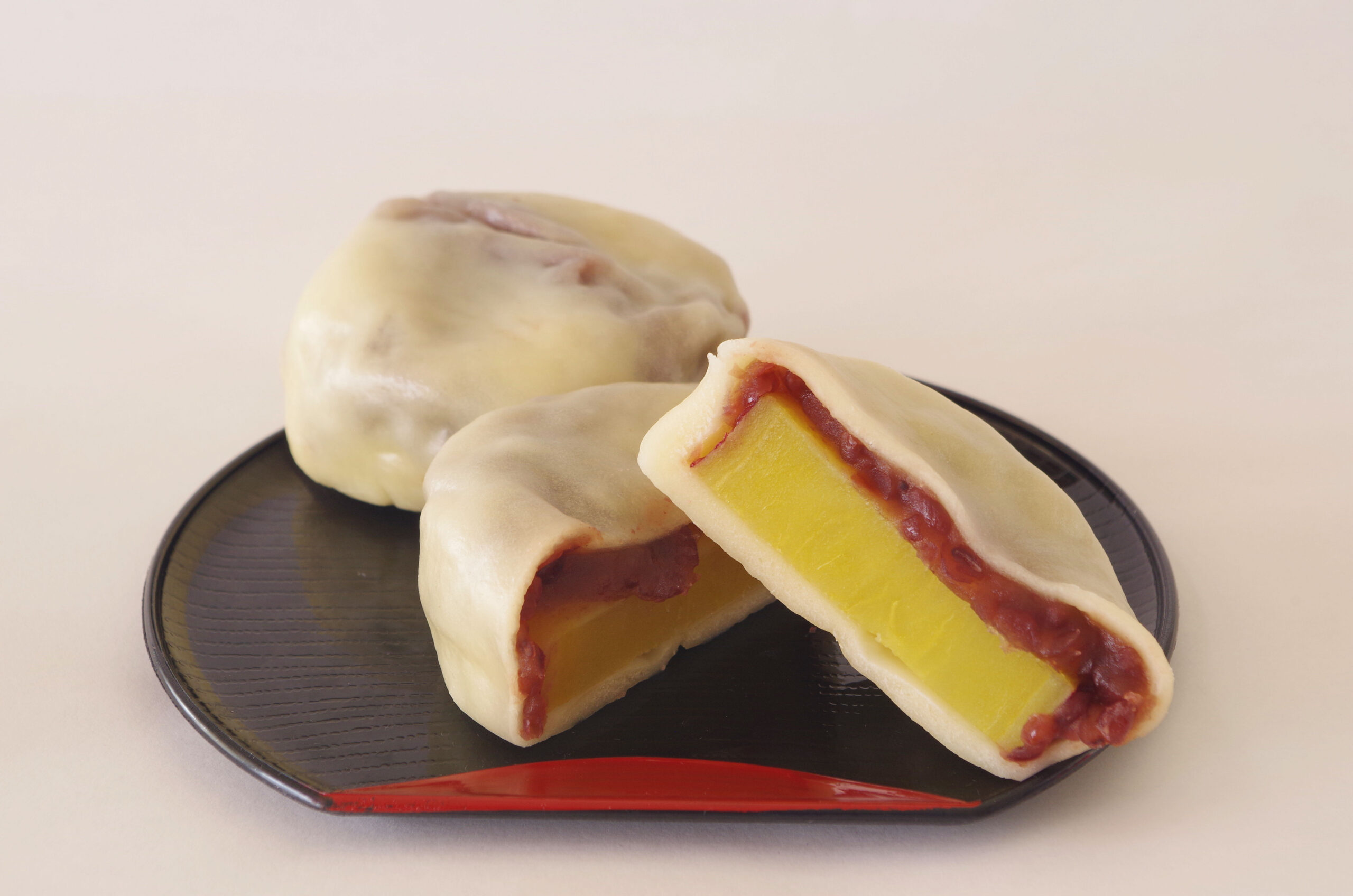 Mochi dumplings with mango and sweet red bean filling on a dark plate, shown from above with a cut piece exposing the yellow mango center and red bean paste.