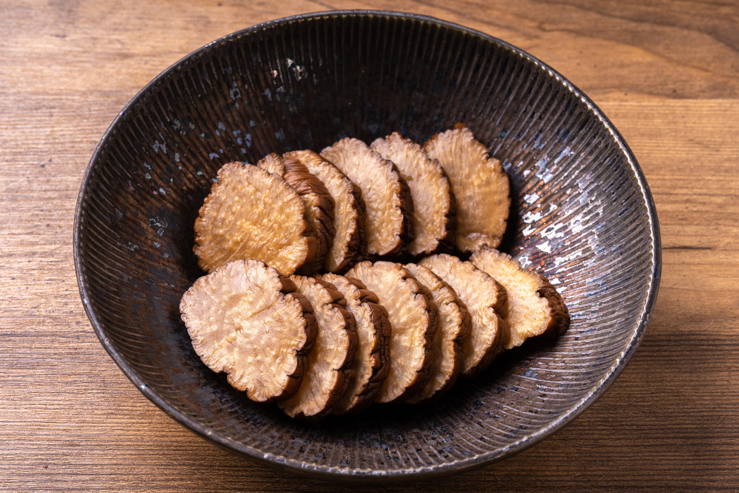 Round, scalloped crackers arranged in a dark ceramic bowl on a wooden table.