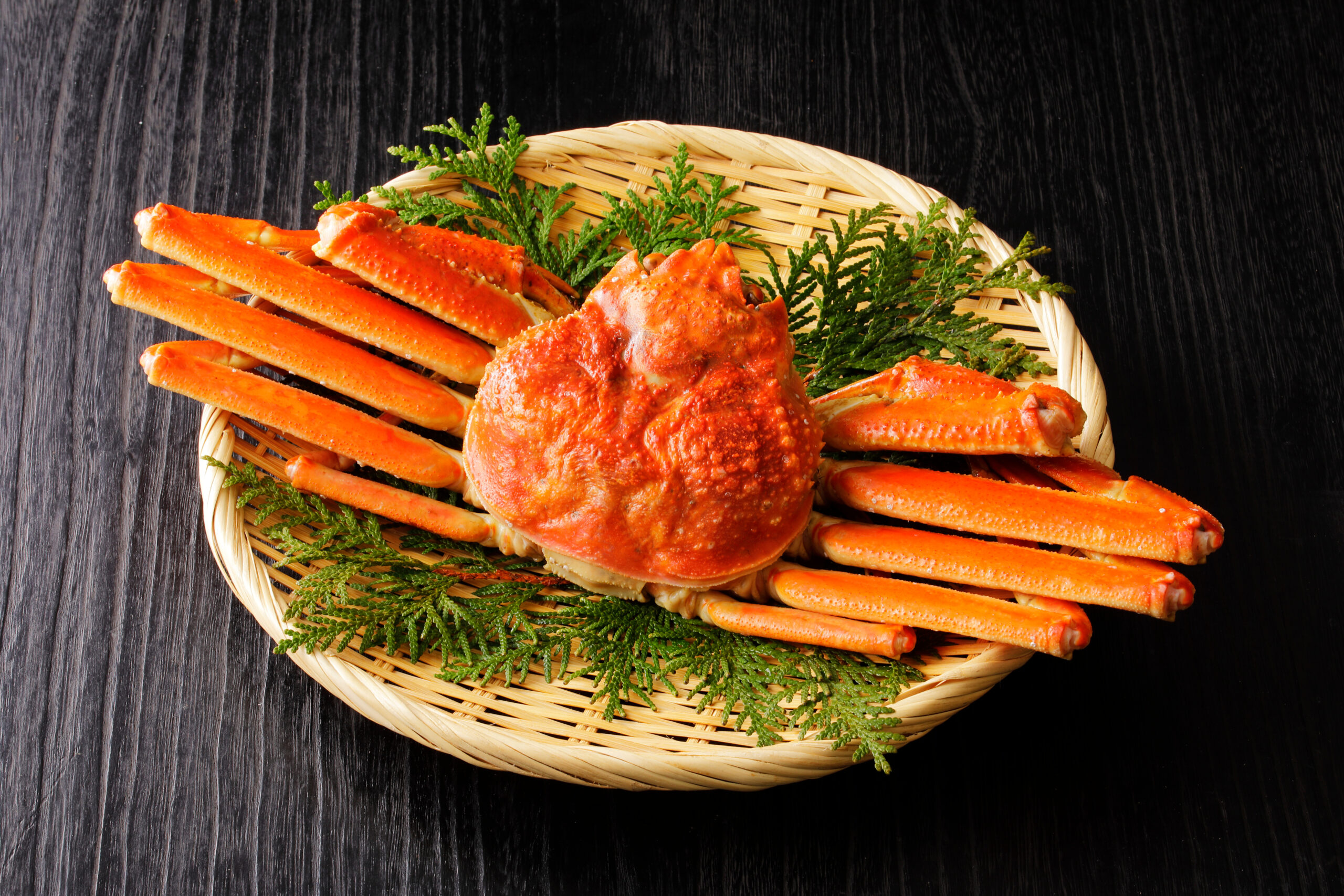 Crab legs arranged in a wicker basket with green garnish on a dark wooden table.