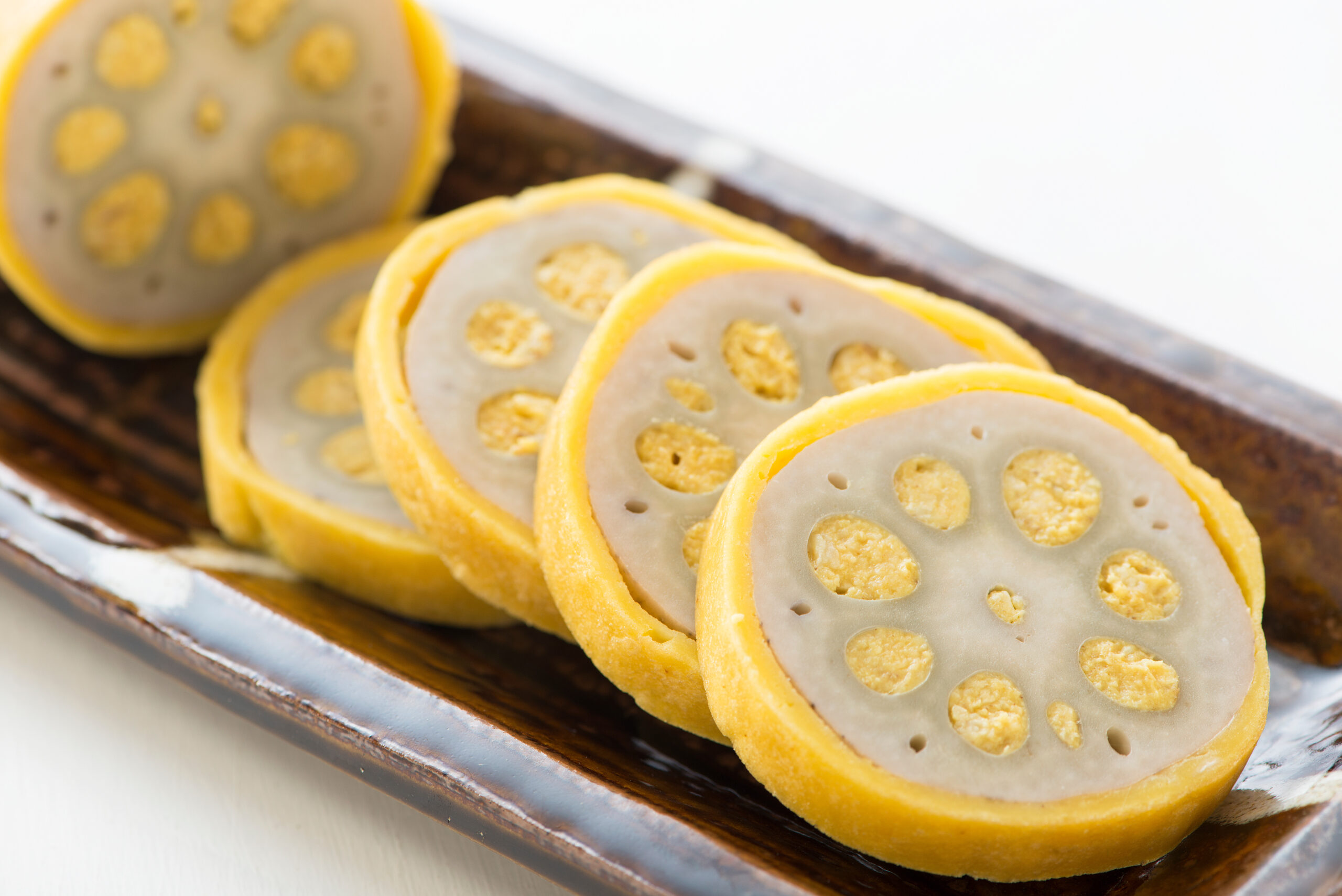 Slices of lotus root with yellow skin on a dark wooden tray, arranged in a row.
