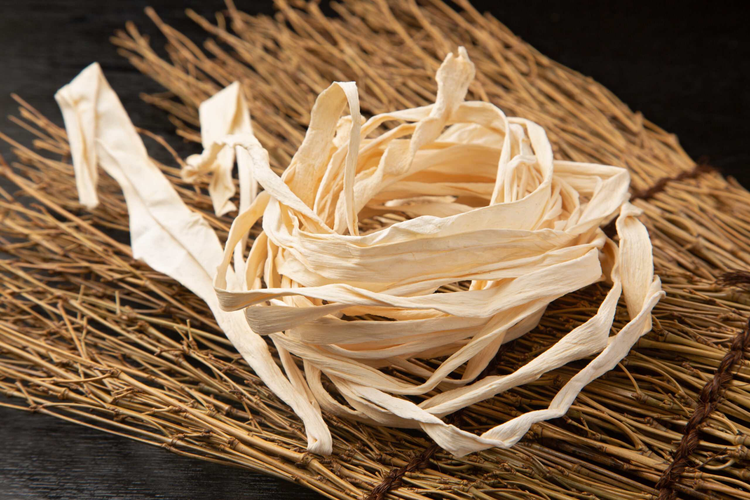 Close-up of pale dried straw or raffia arranged in a nest-like formation on a dark wooden surface.