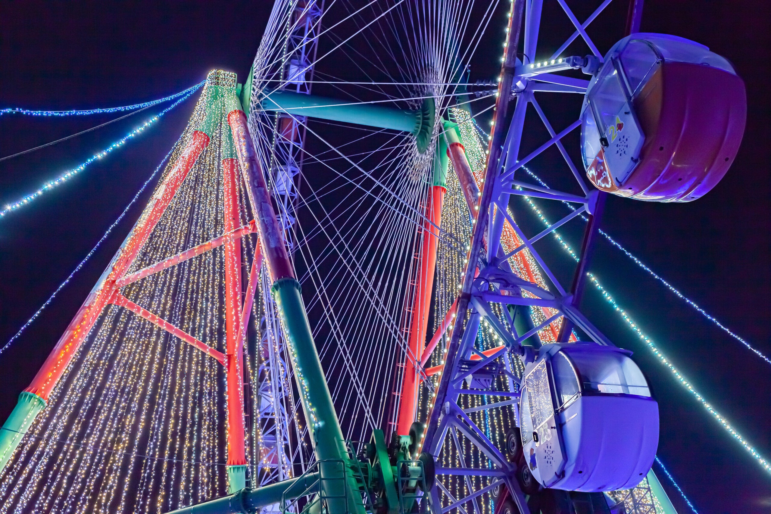 Close-up of a brightly lit Ferris wheel at night with colorful illuminated spokes and strings of lights
