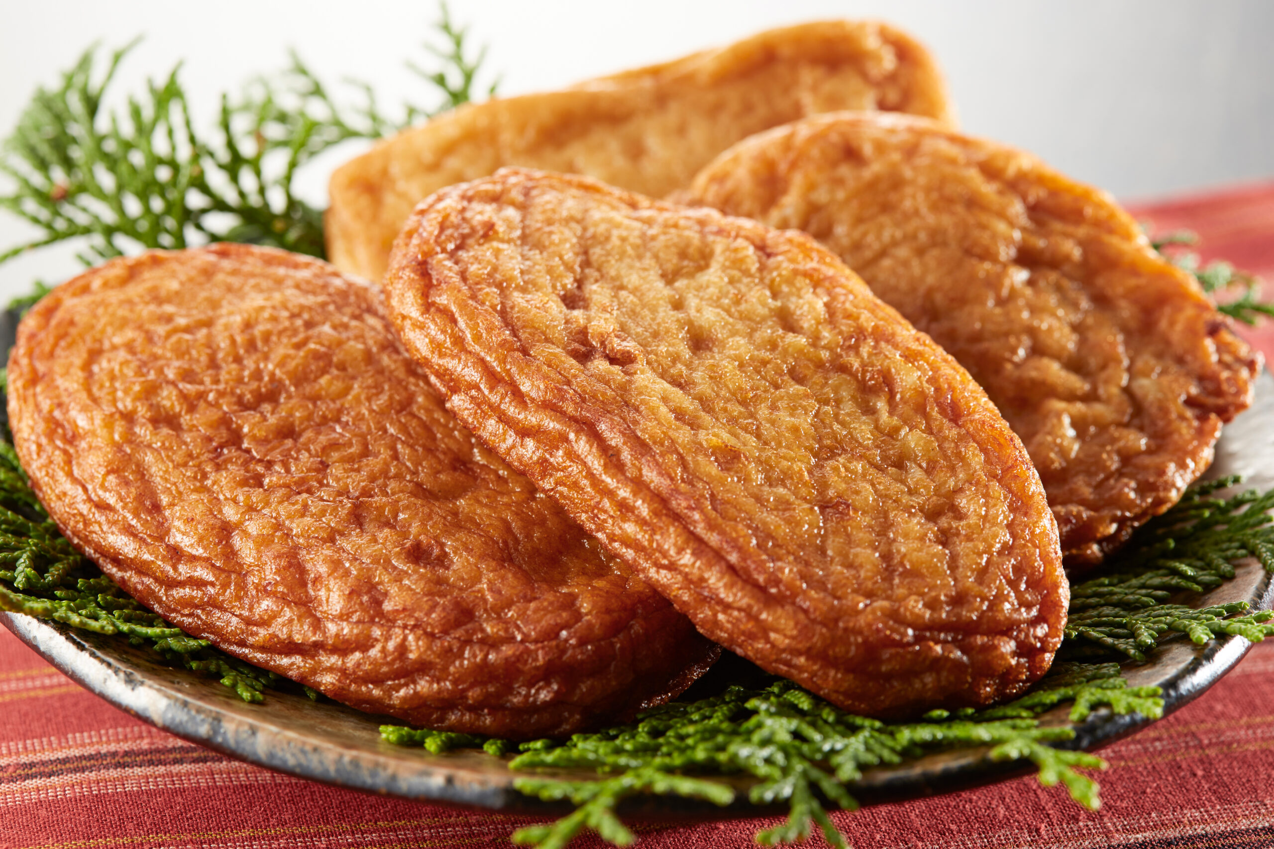 Stack of golden brown fried pastries on a plate with green garnish in the background