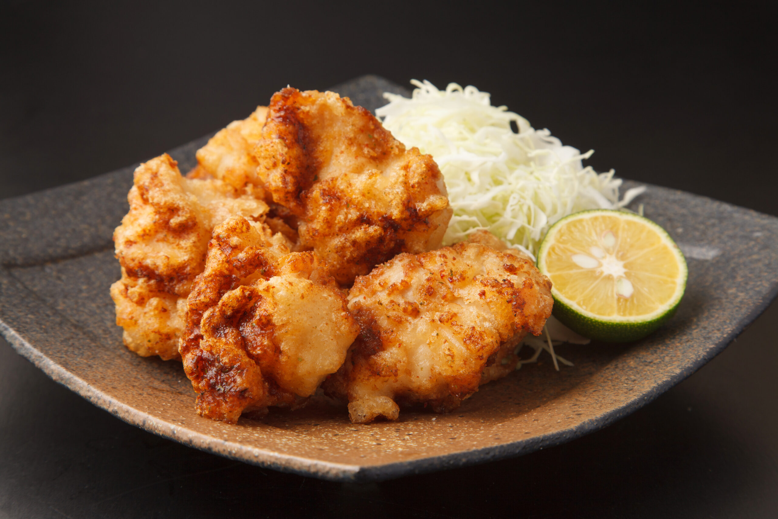 Crispy fried chicken pieces on a plate with shredded cabbage and lime wedges as garnish.