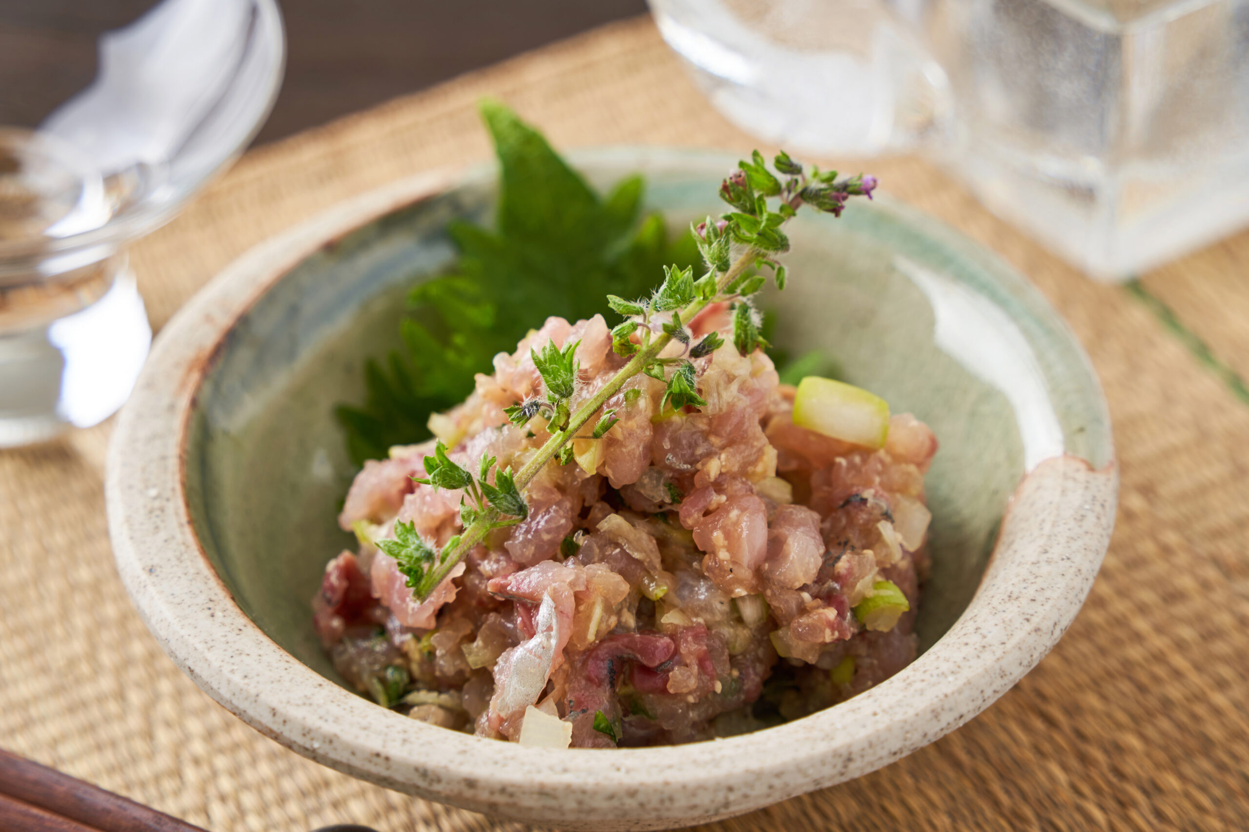 Beef tartare topped with fresh herb sprigs in a rustic ceramic bowl on a wooden table.