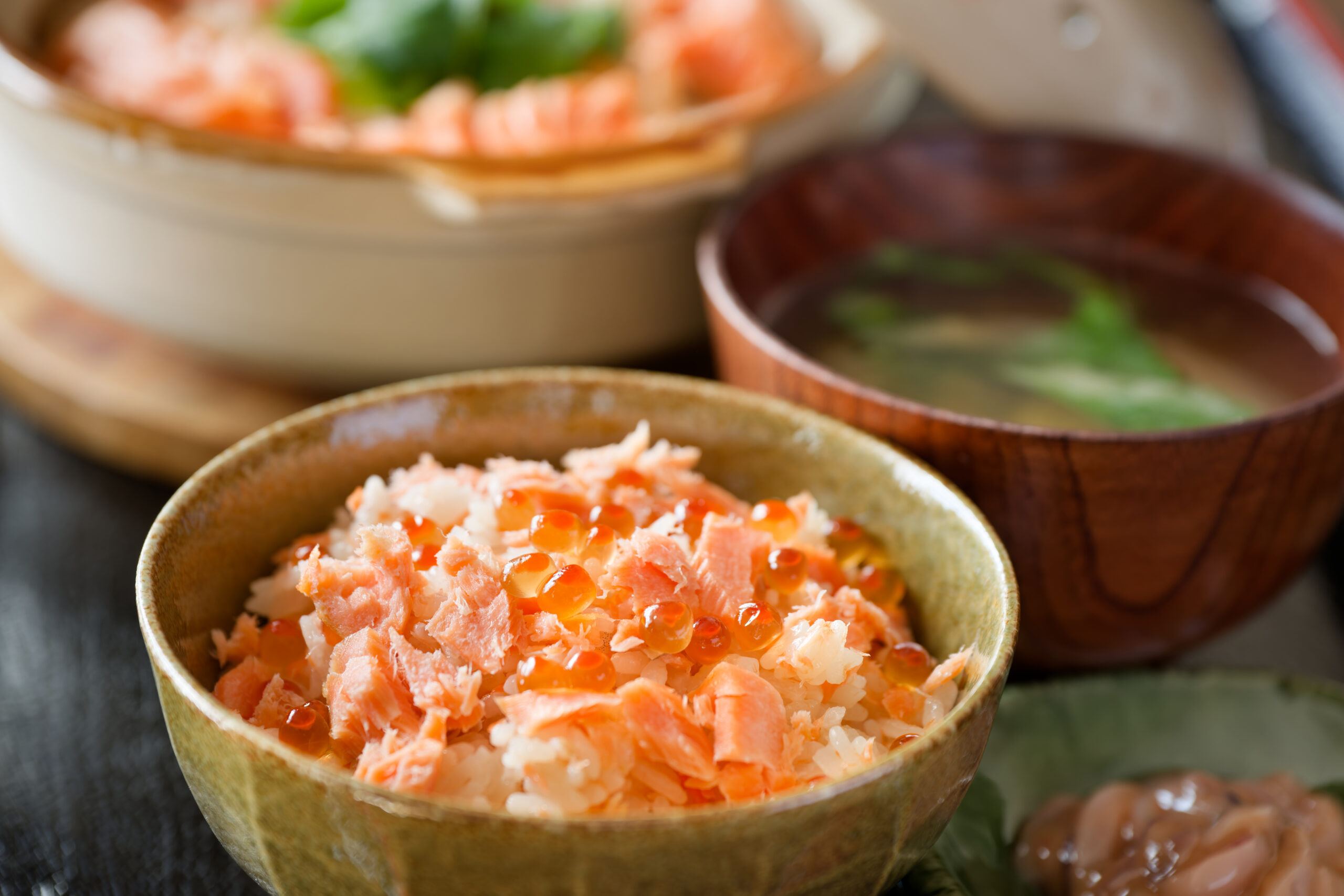 Close-up of a bowl of salmon flakes with salmon roe on rice, with other bowls blurred in the background (Japanese donburi).