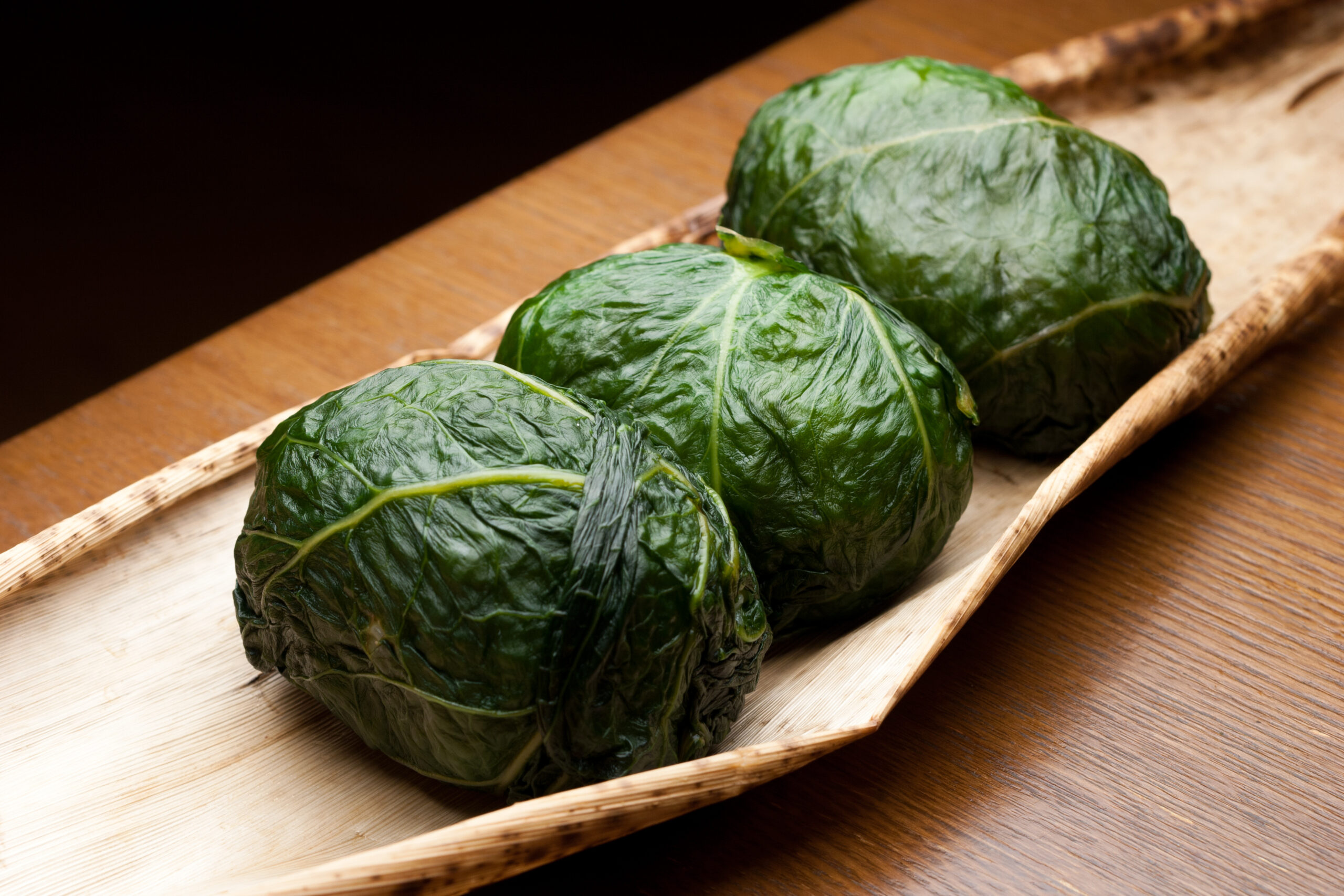 Three green cabbage heads resting on a light wooden tray.
