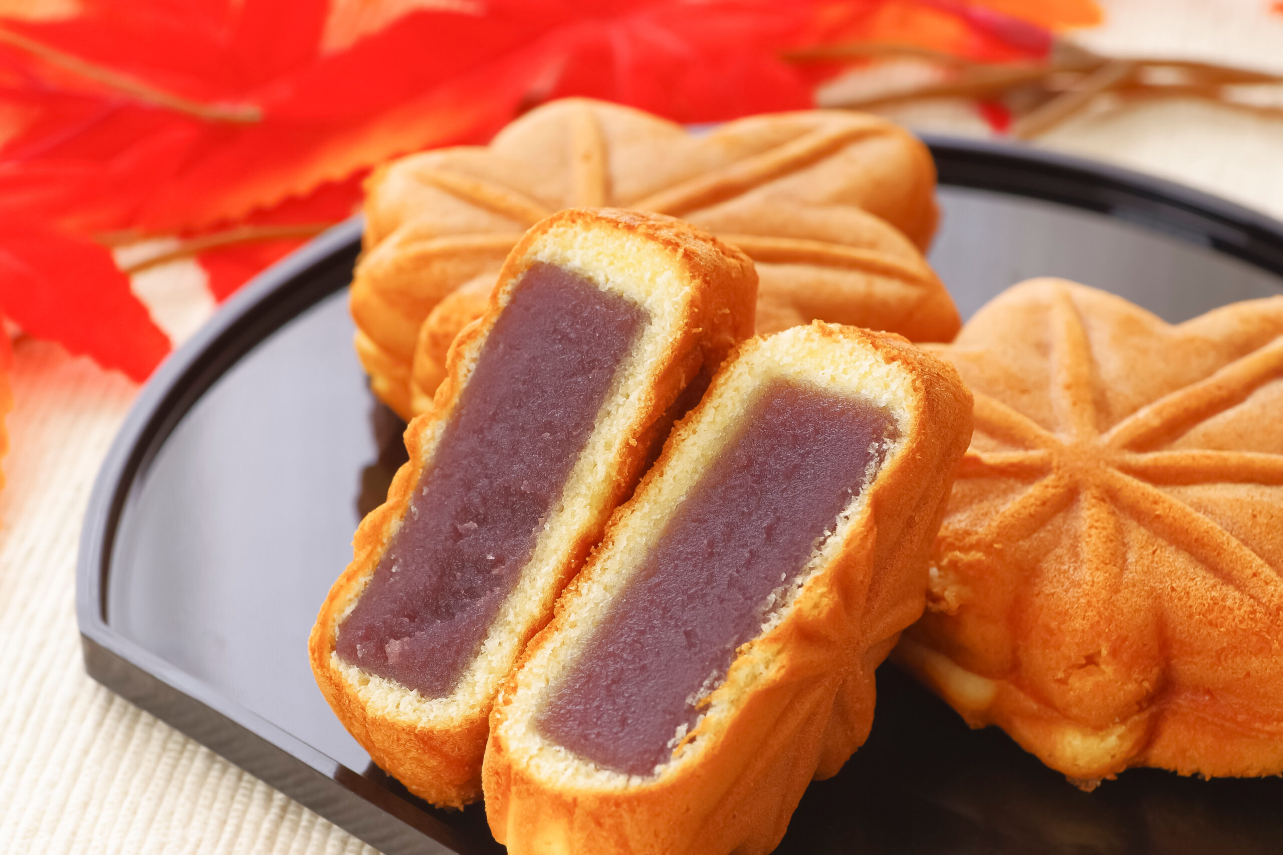 Sliced pastry with purple filling on a dark tray, red autumn leaves in the background.