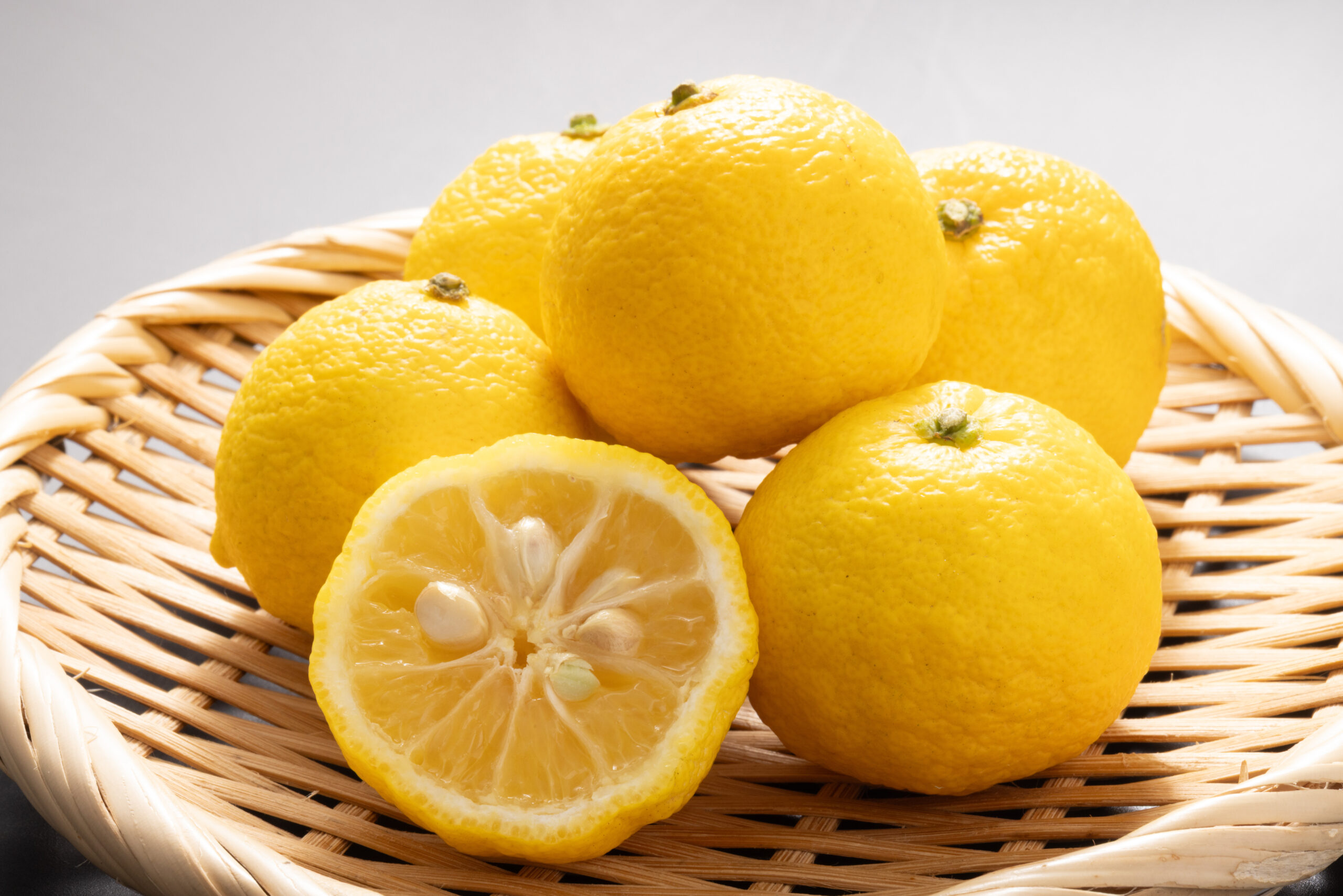Bright yellow lemons piled in a wicker basket, with one lemon cut in half showing juicy segments and seeds in the foreground