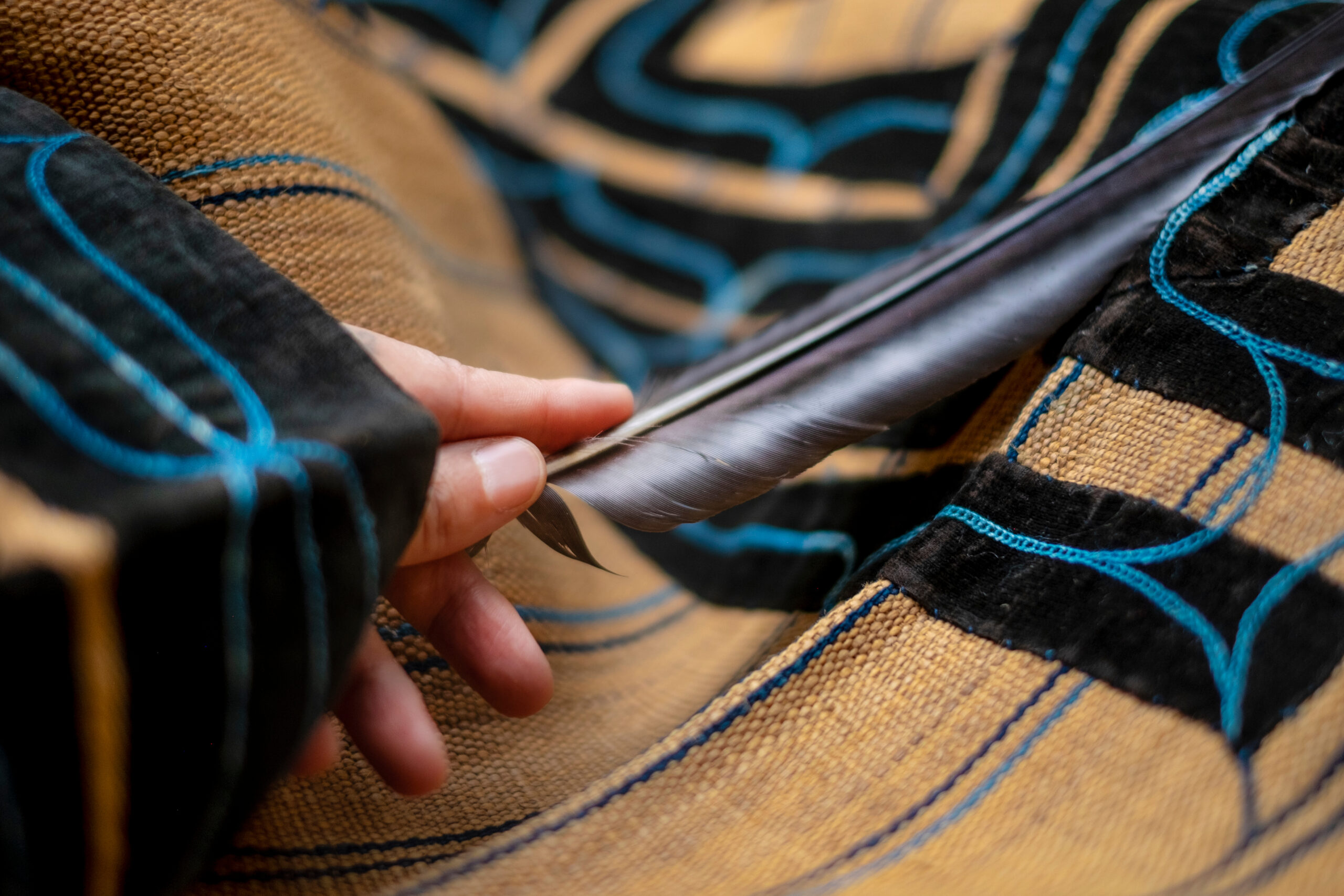 Close-up of a hand pulling apart a zipper along a khaki fabric with blue stitching on a jacket.