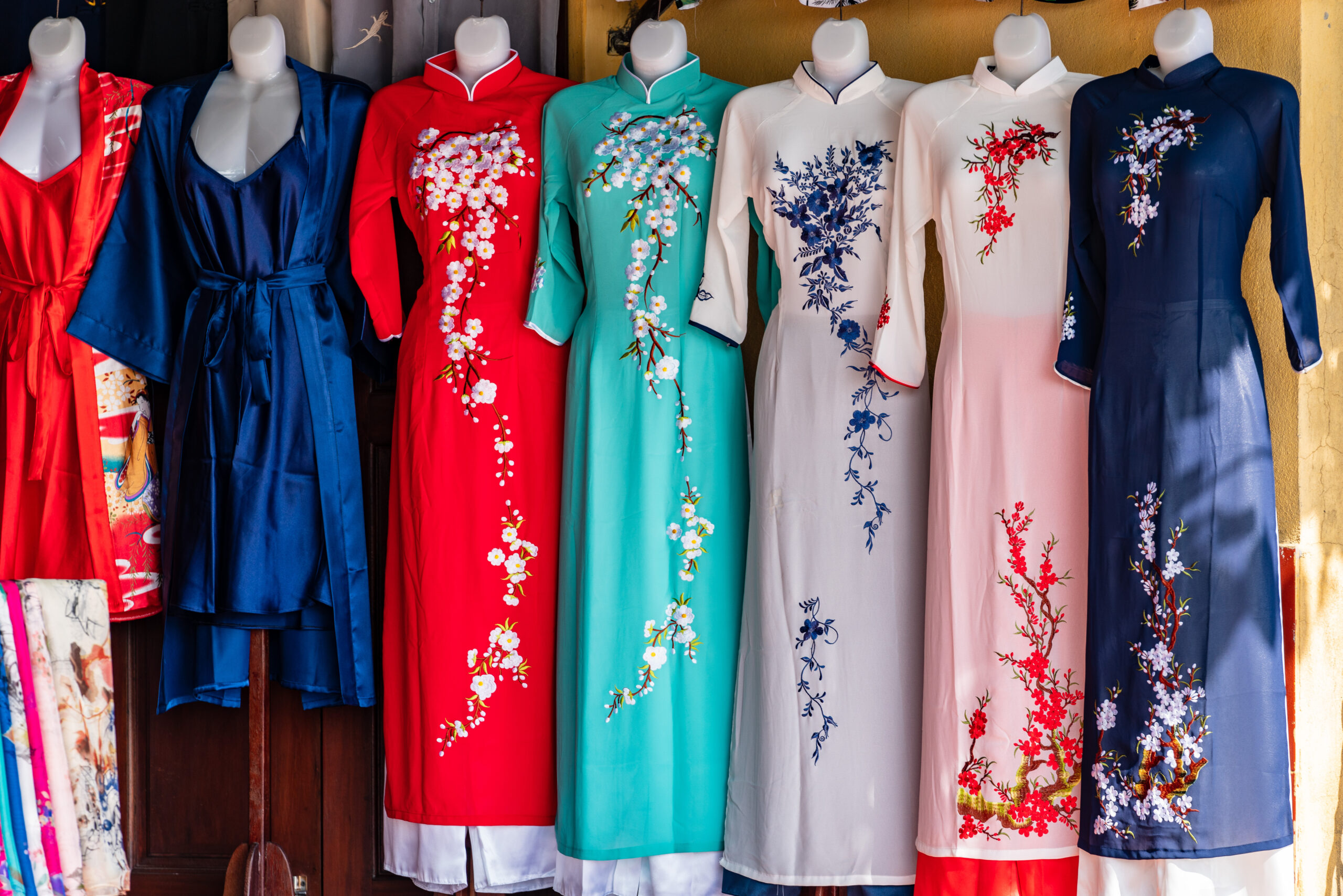 Row of bright, embroidered dresses hanging side by side in red, blue, teal, white, pink and navy colors.
