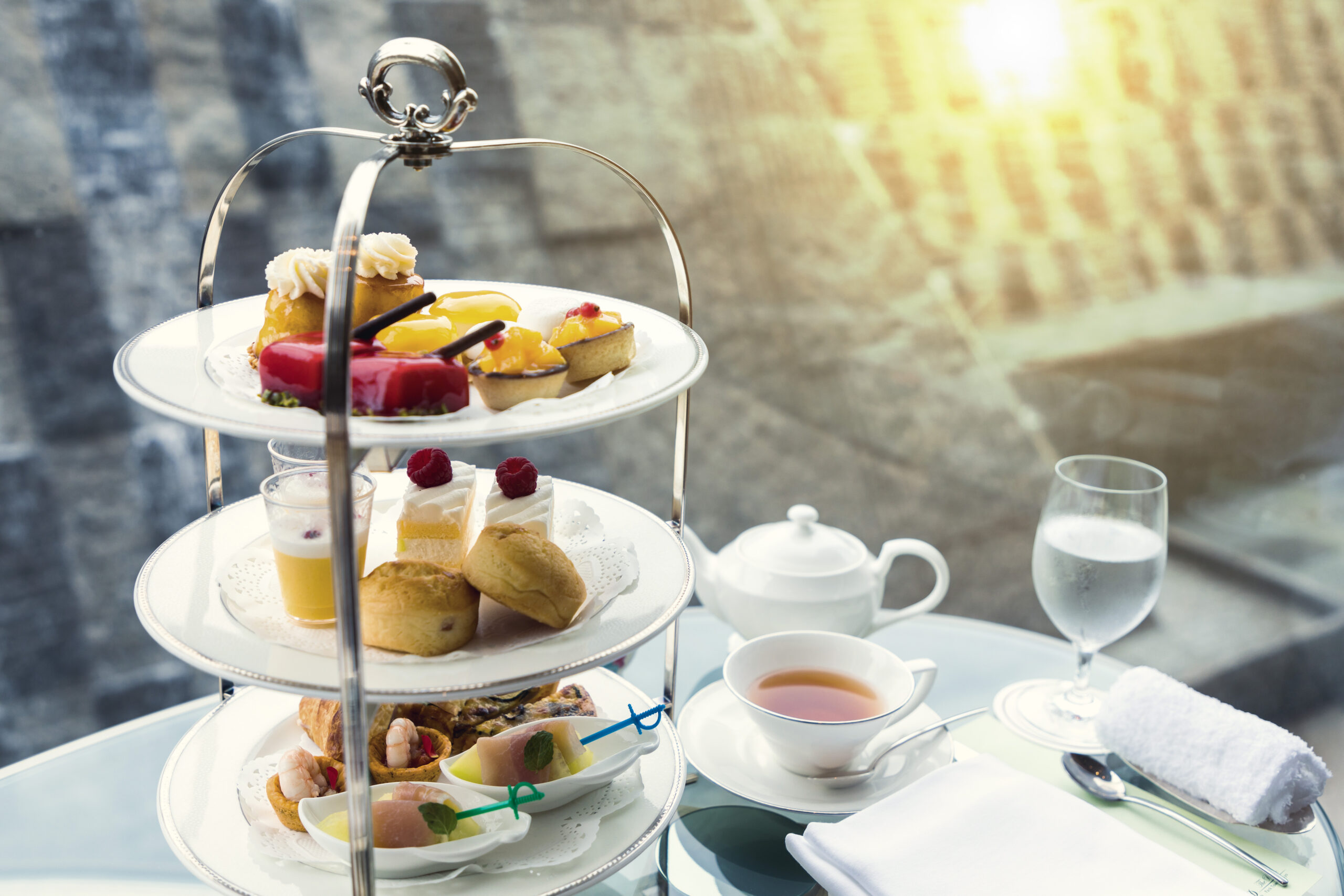 Three-tiered silver dessert stand with assorted pastries and cakes for afternoon tea.