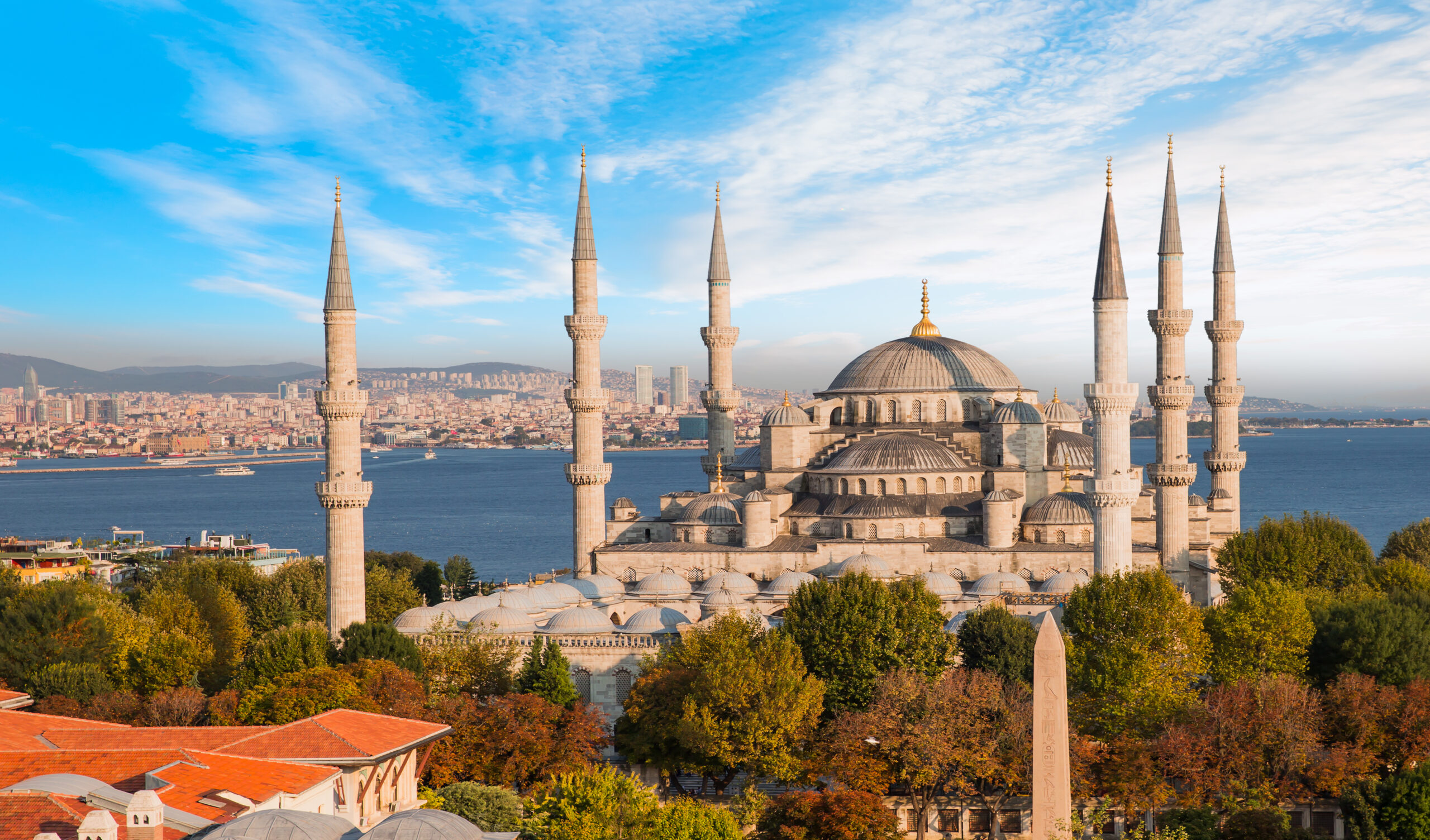 The Blue Mosque in Istanbul with six minarets and a central dome against a clear blue sky and Bosphorus backdrop.