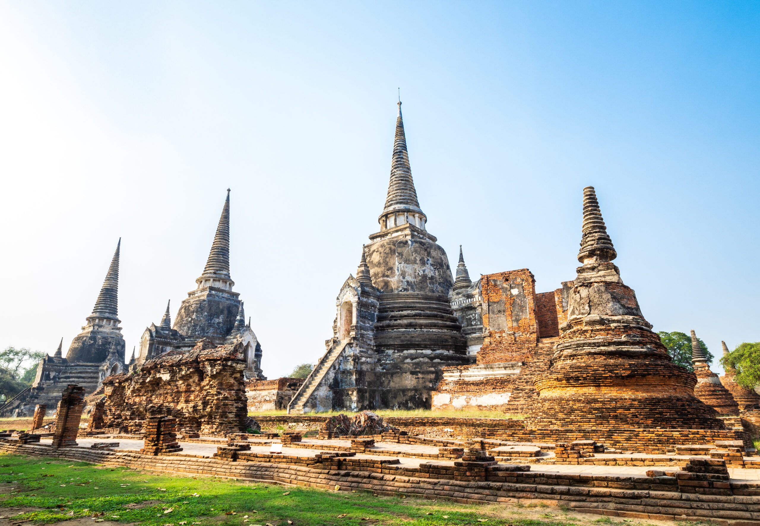 Ancient temple complex with weathered stone stupas and brick platforms under a clear blue sky.