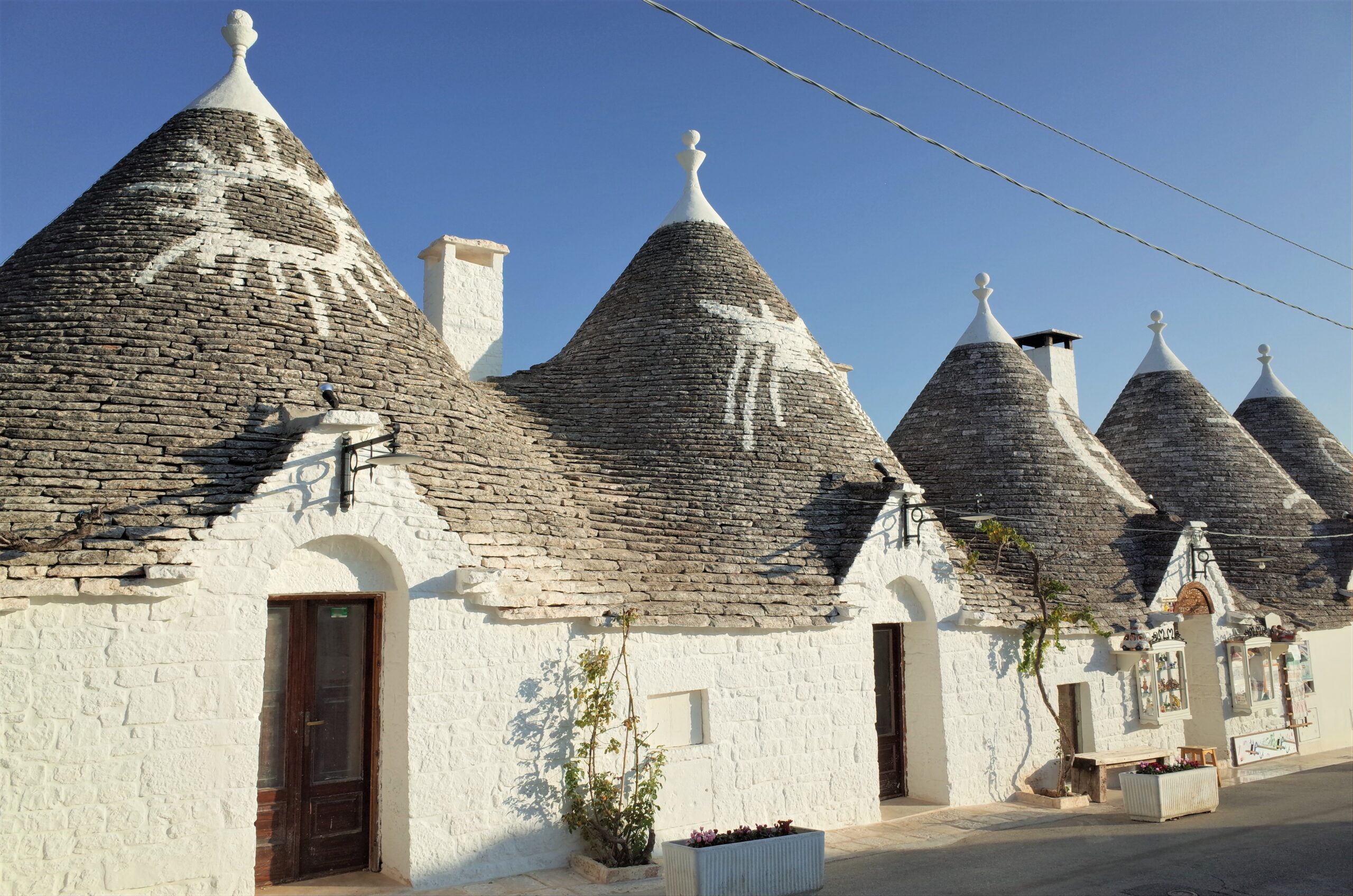 Whitewashed trulli houses with conical stone roofs along a sunny street.