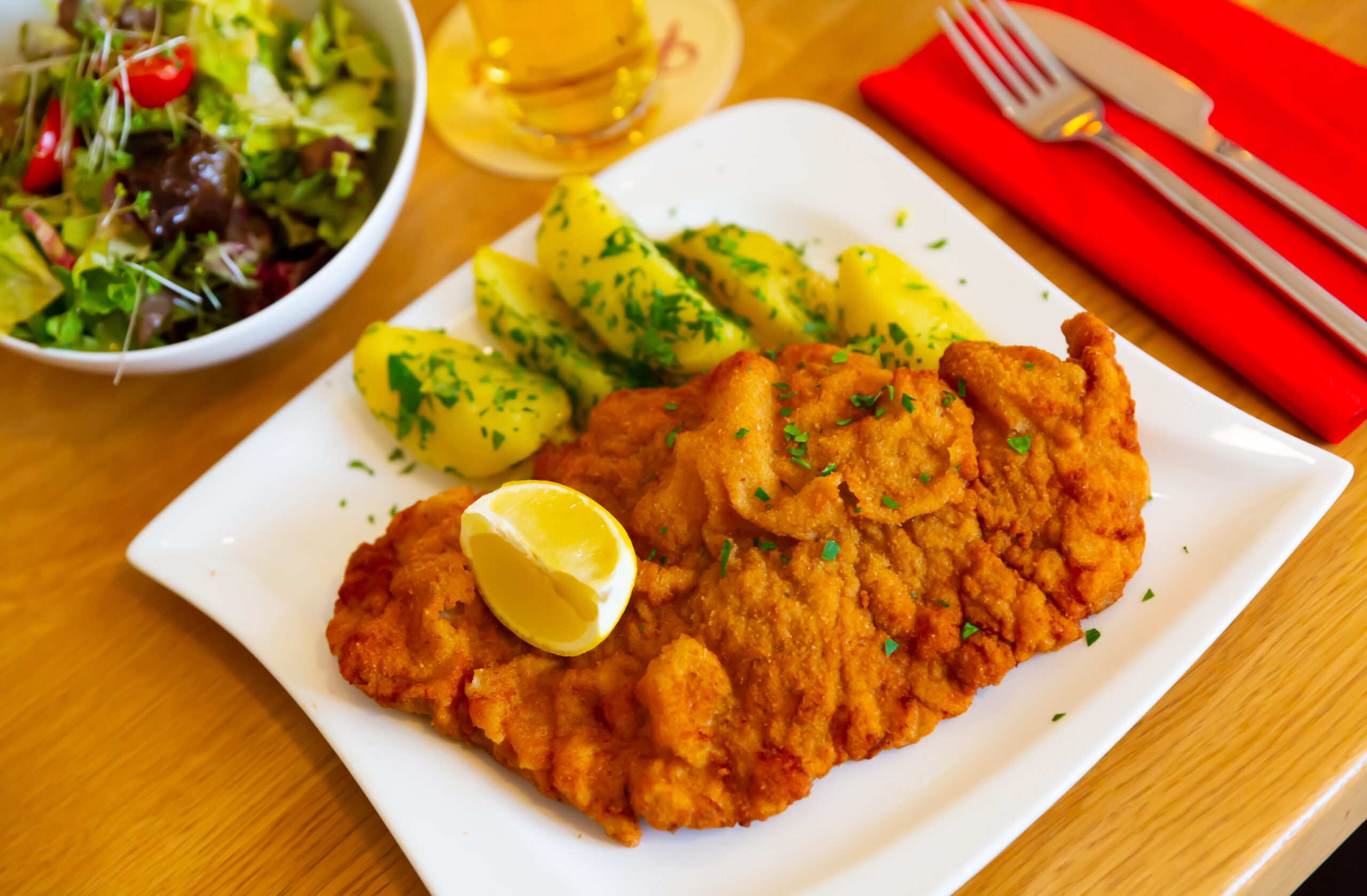 Golden fried chicken fillet with parsley, served with boiled potatoes and a side salad on a white plate.