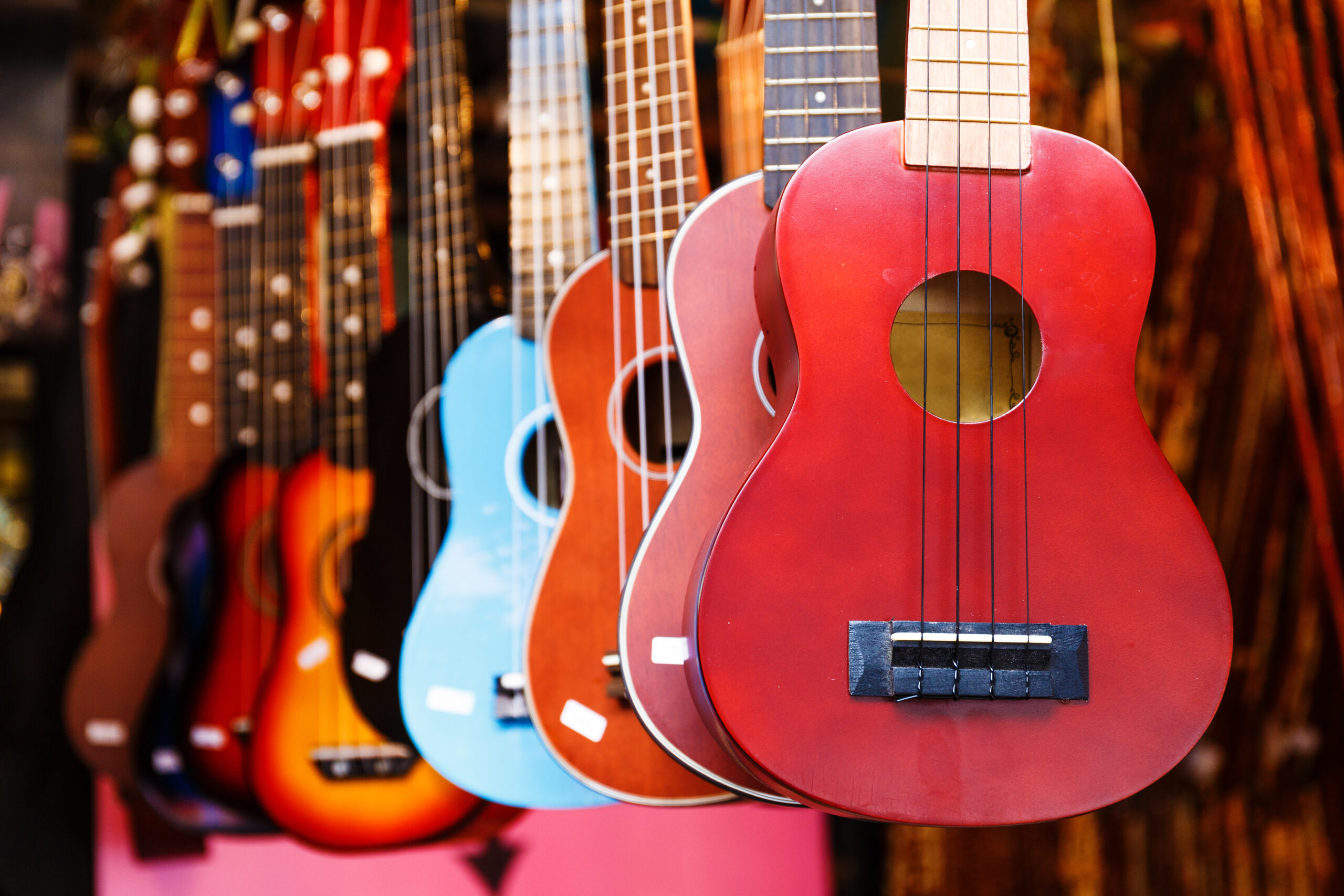 Red acoustic guitar in the foreground with a row of colorful guitars hanging in a music-store display in the background.