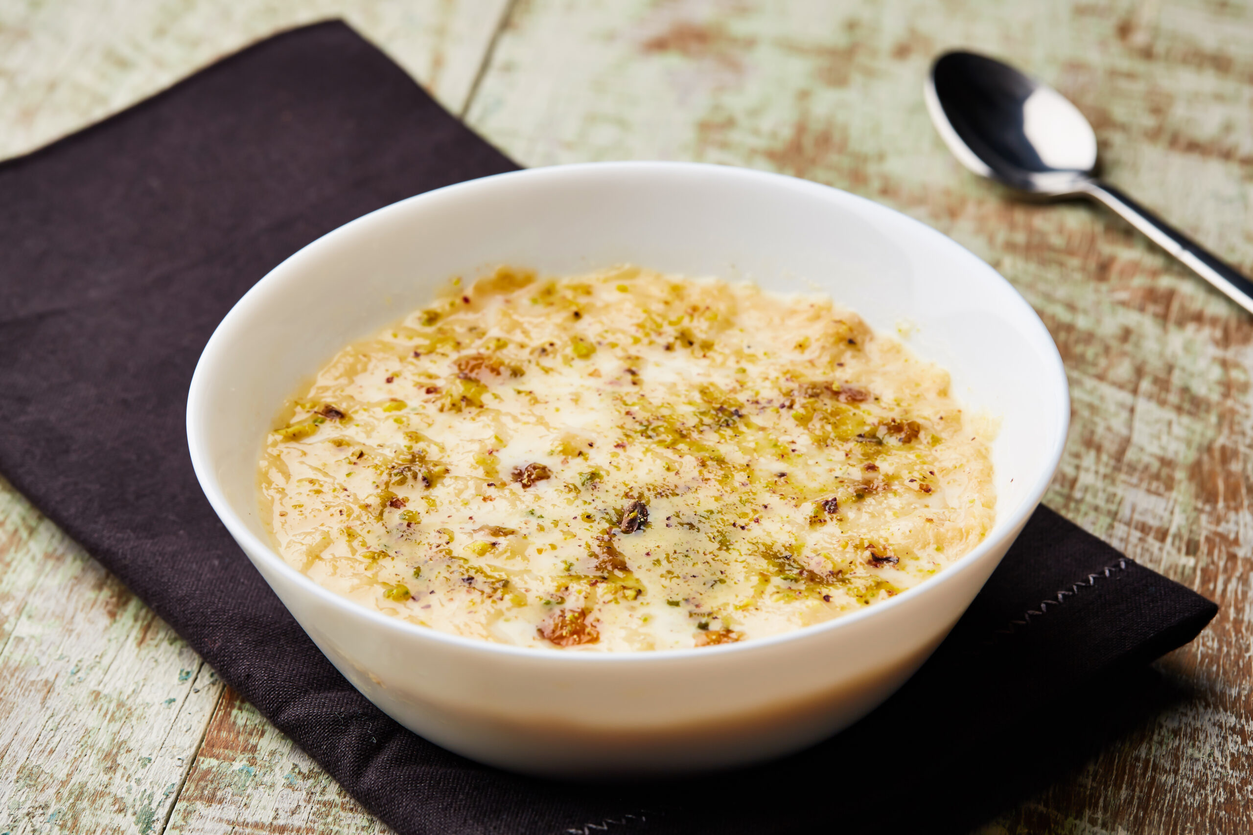 Creamy pudding topped with chopped pistachios in a white bowl on a rustic wooden table