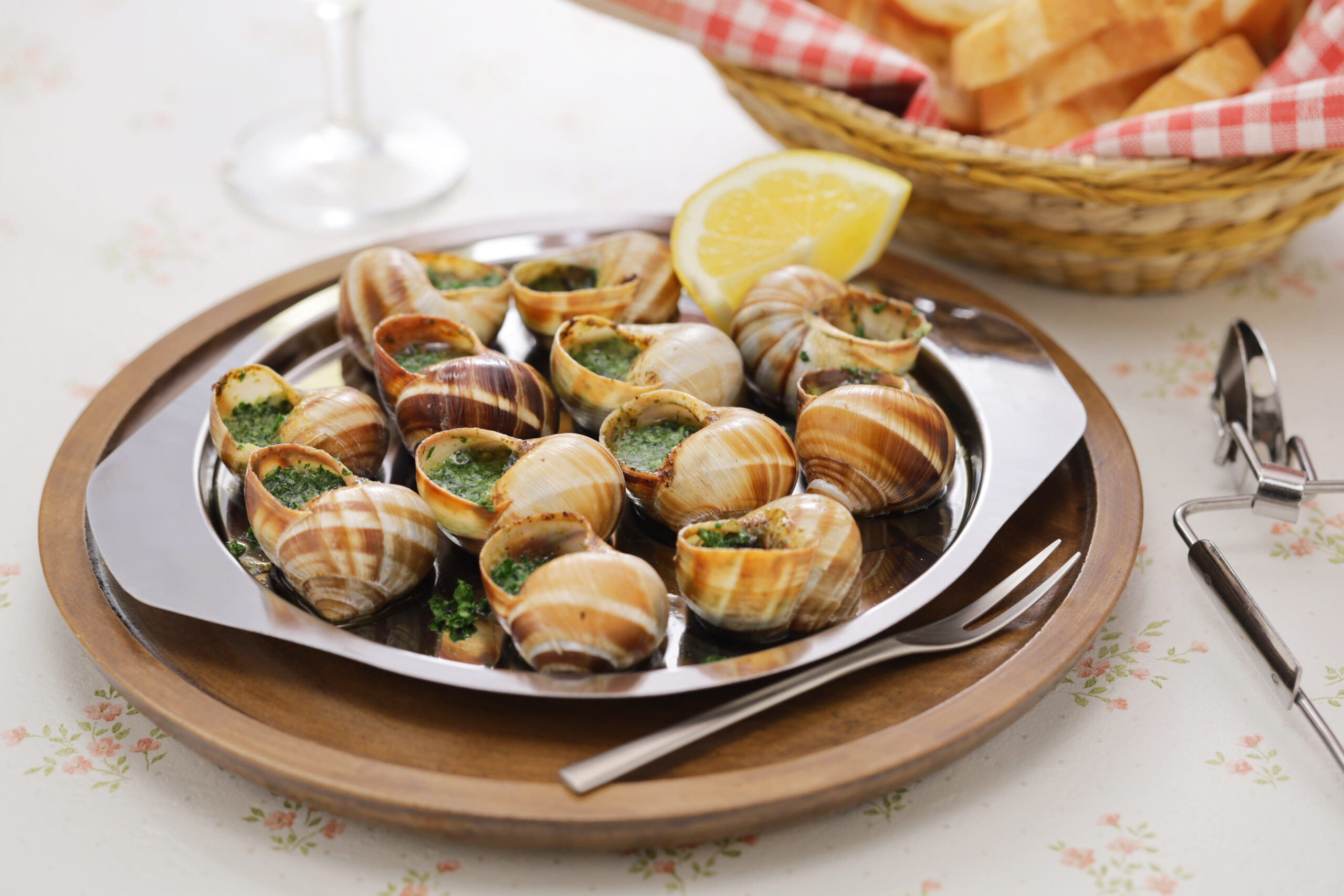 Clams stuffed with green herb filling on a silver platter with a lemon wedge in the background.