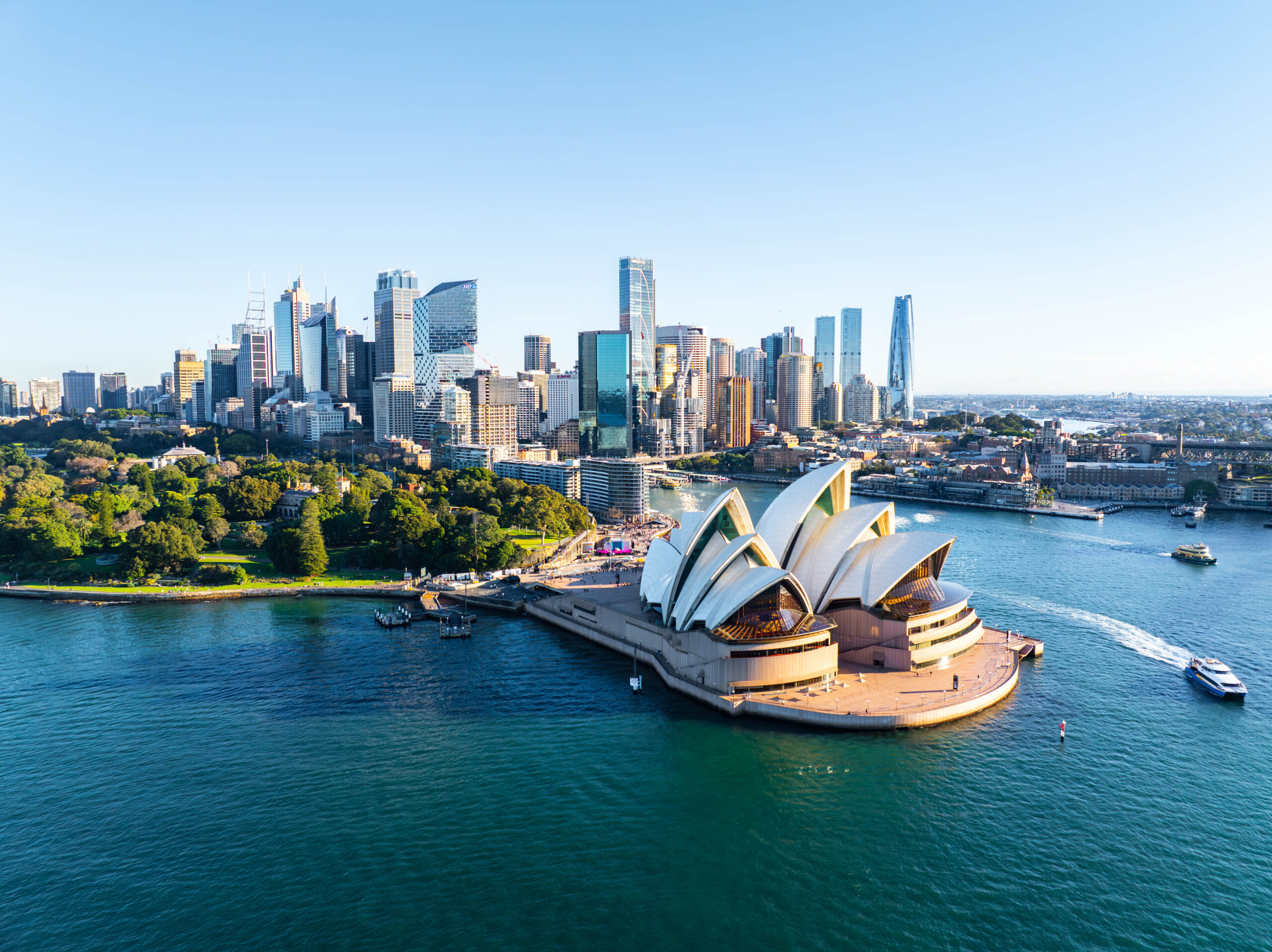 Sydney skyline with the Opera House and circular harborfront in the foreground under a clear blue sky