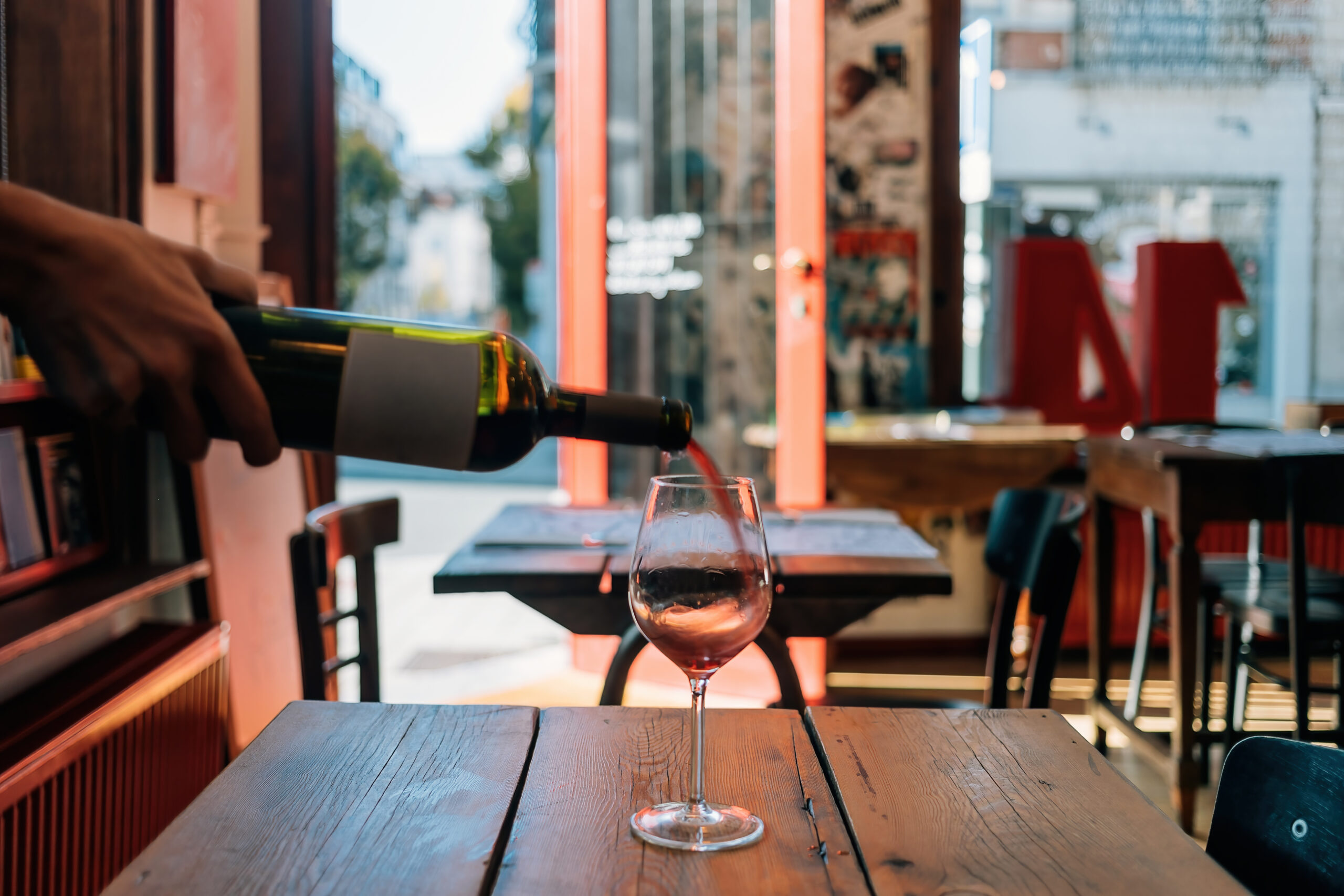 Wine being poured from a bottle into a wine glass on a wooden table at a restaurant.