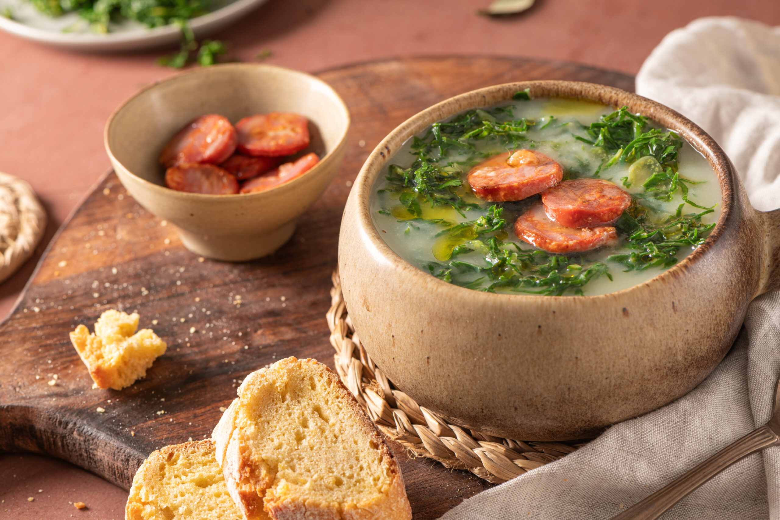 Rustic bowl of creamy sausage and greens soup with sliced sausage and bread on a wooden table.