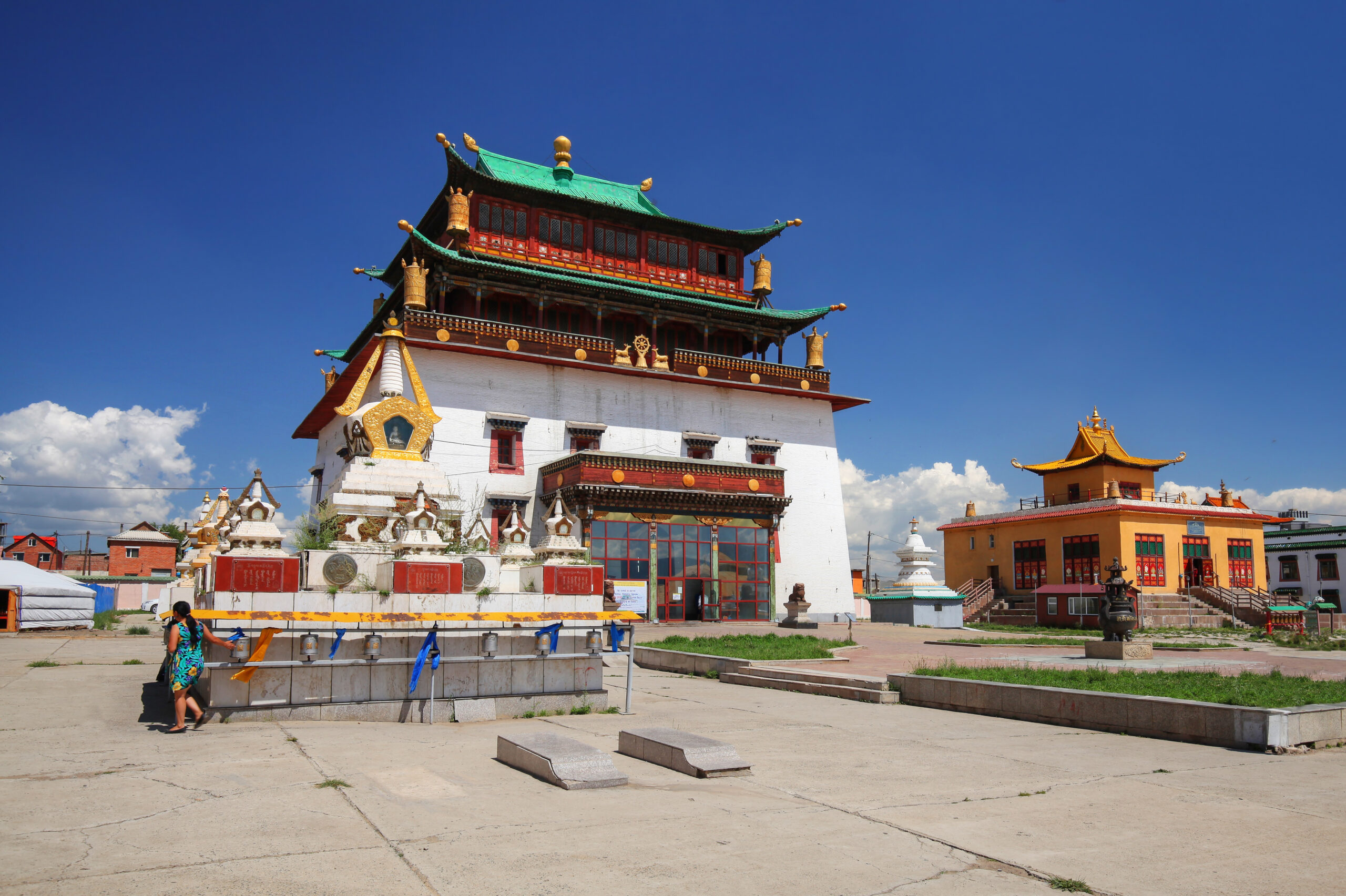 Colorful multi-tiered Asian temple with green roofs, red walls, and gold ornaments under a bright blue sky.