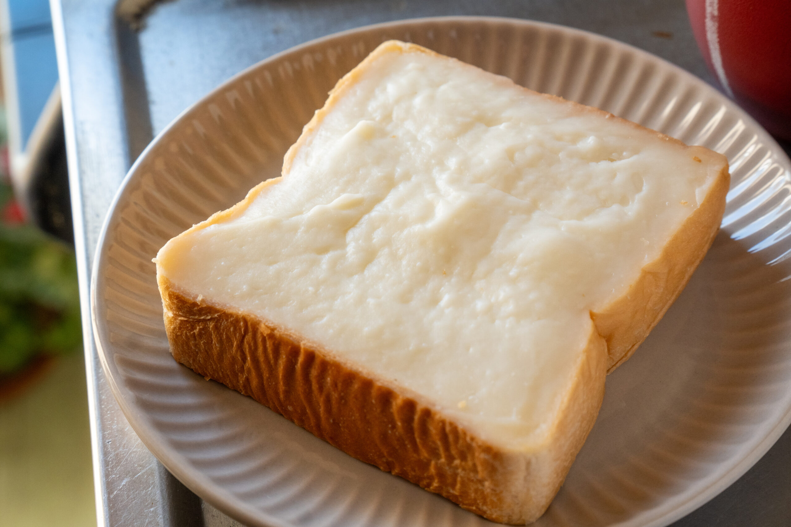 Two slices of white bread with butter spread on top, placed on a light-colored plate outdoors or on a metal surface