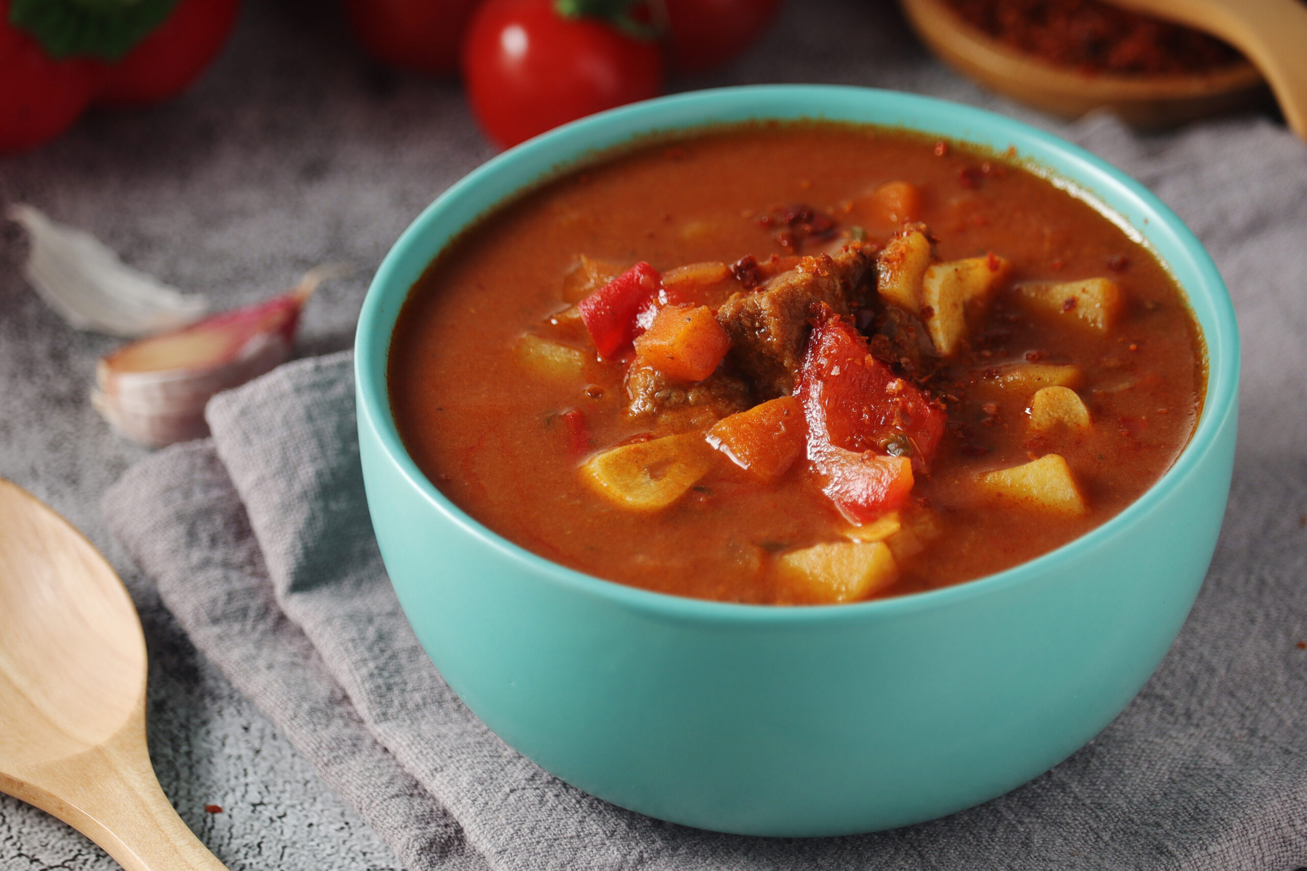 Hearty beef stew with potatoes and red bell peppers in a turquoise bowl, on a gray table.