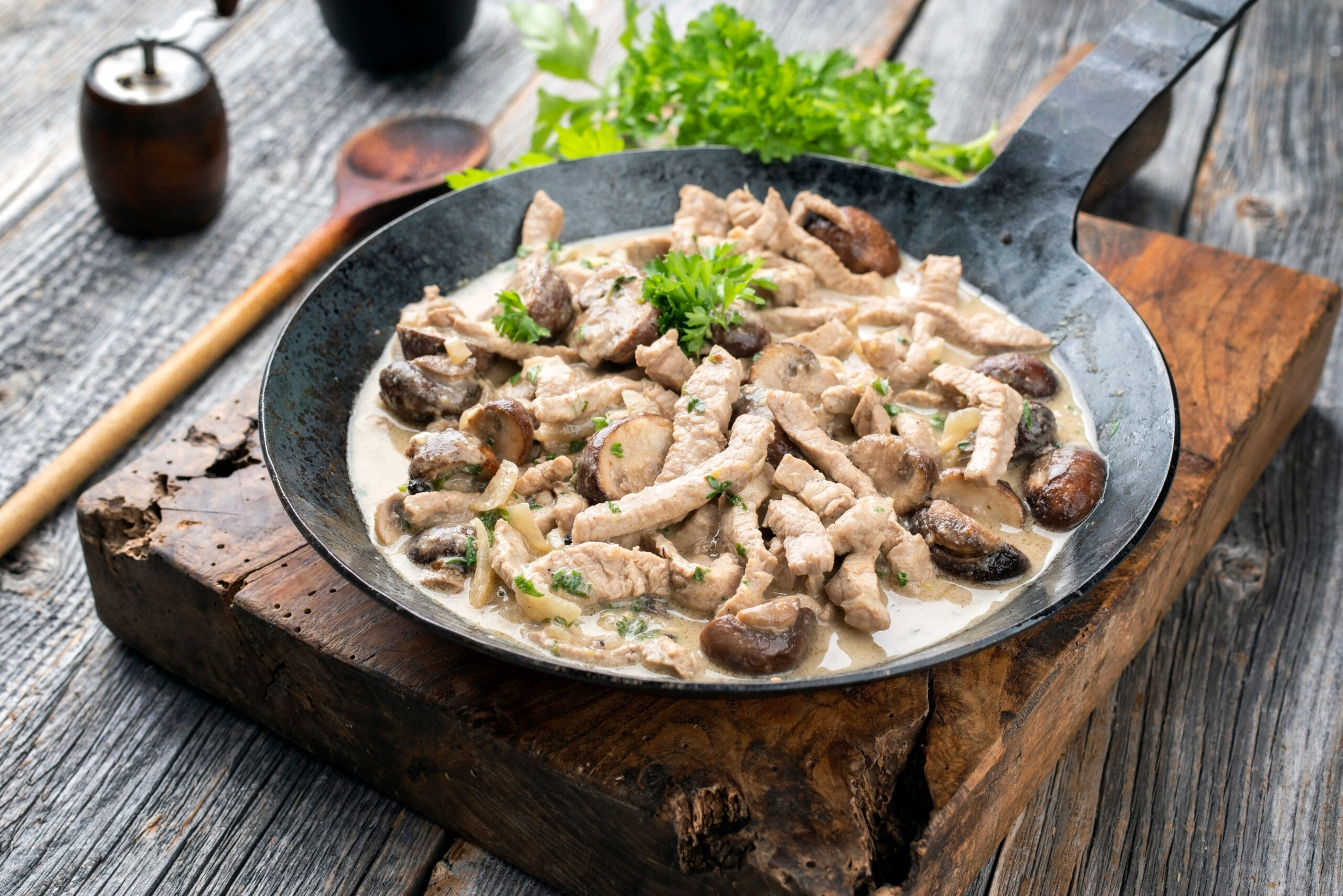 Creamy chicken and mushroom skillet garnished with parsley on a rustic wooden table inside a heavy black pan