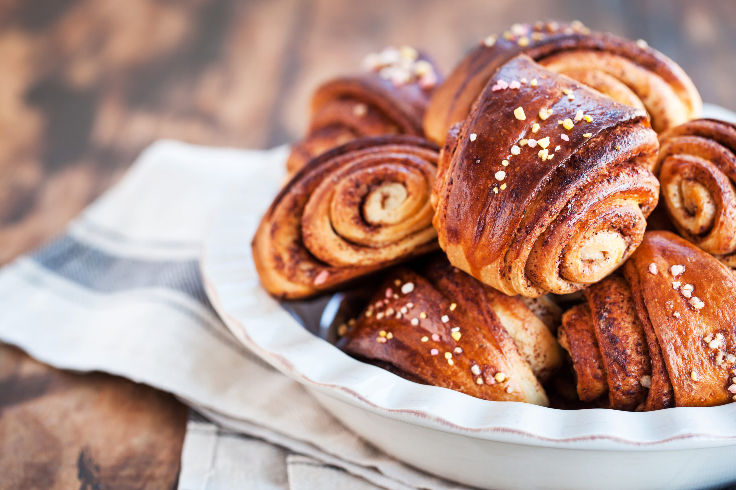 Close-up of glossy cinnamon rolls with sugar crystals on parchment, showcasing golden-brown swirls and flaky texture.