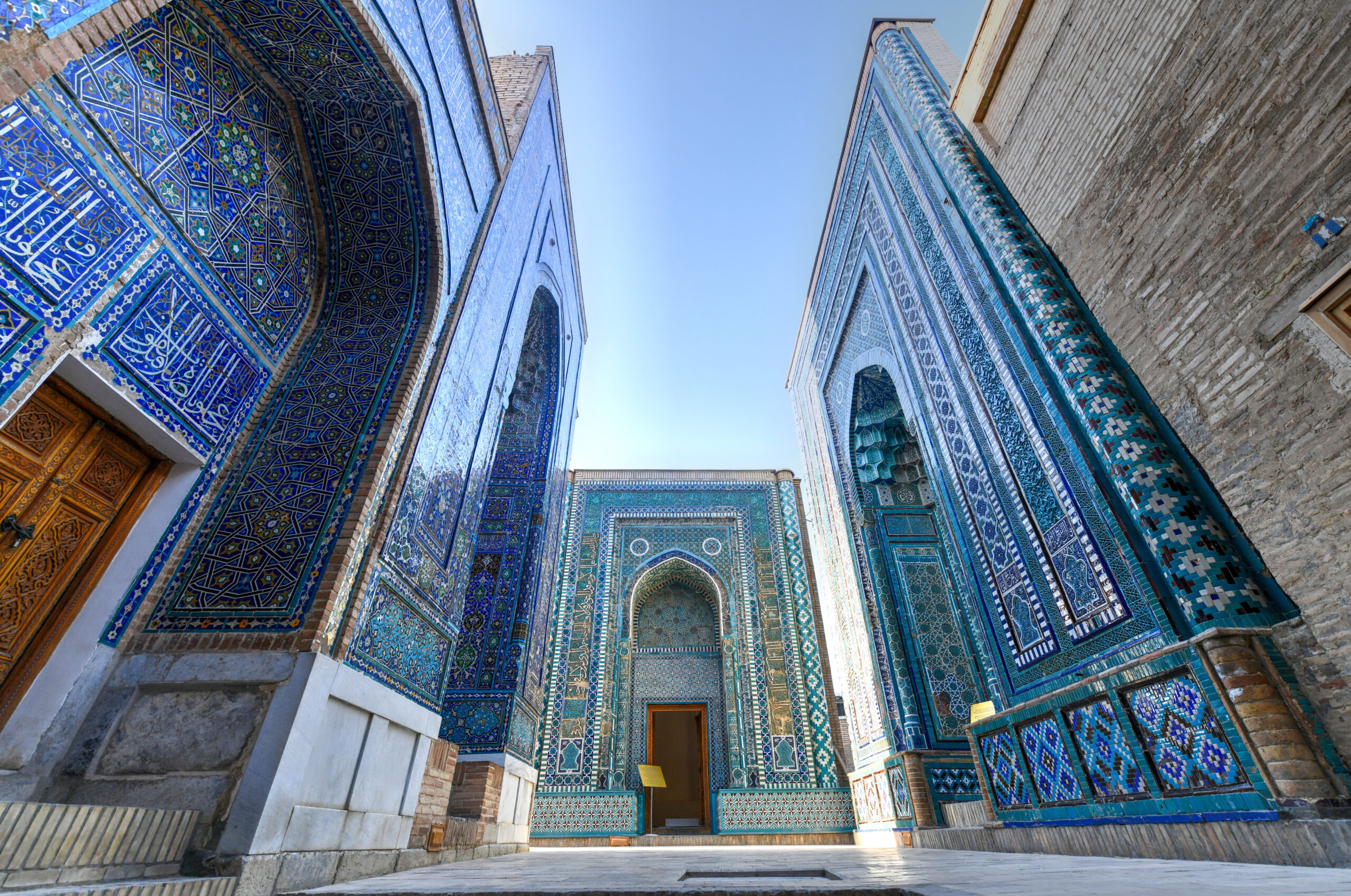 Blue mosaic tiled walls with intricate geometric arabesque patterns framing an arched doorway of a historic building.