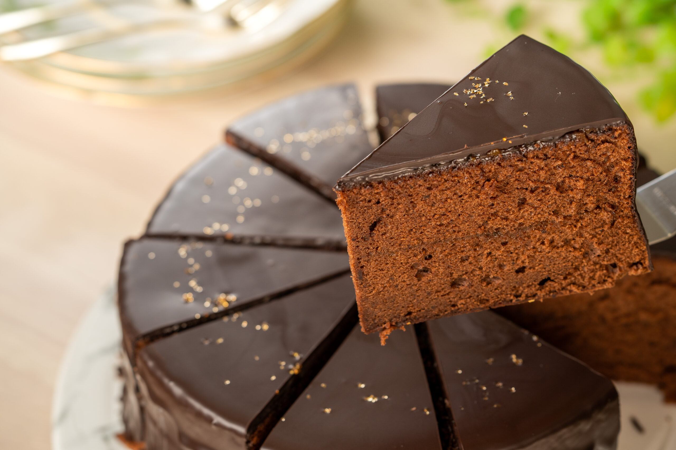 Slice of rich chocolate cake with glossy ganache on a plate, crumbs sprinkled around.