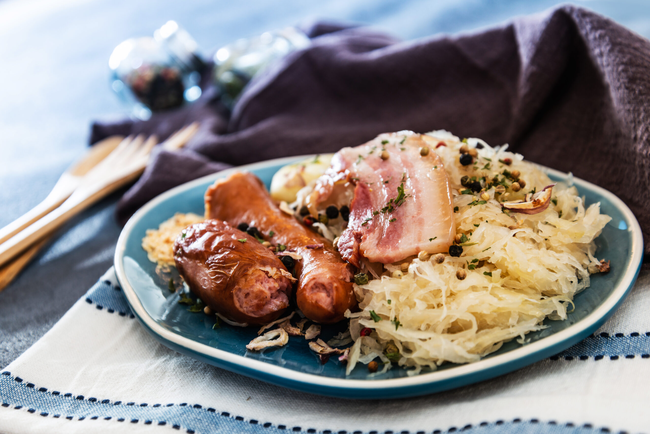 Plate with sausages and bacon on sauerkraut, garnished with herbs on a blue plate.