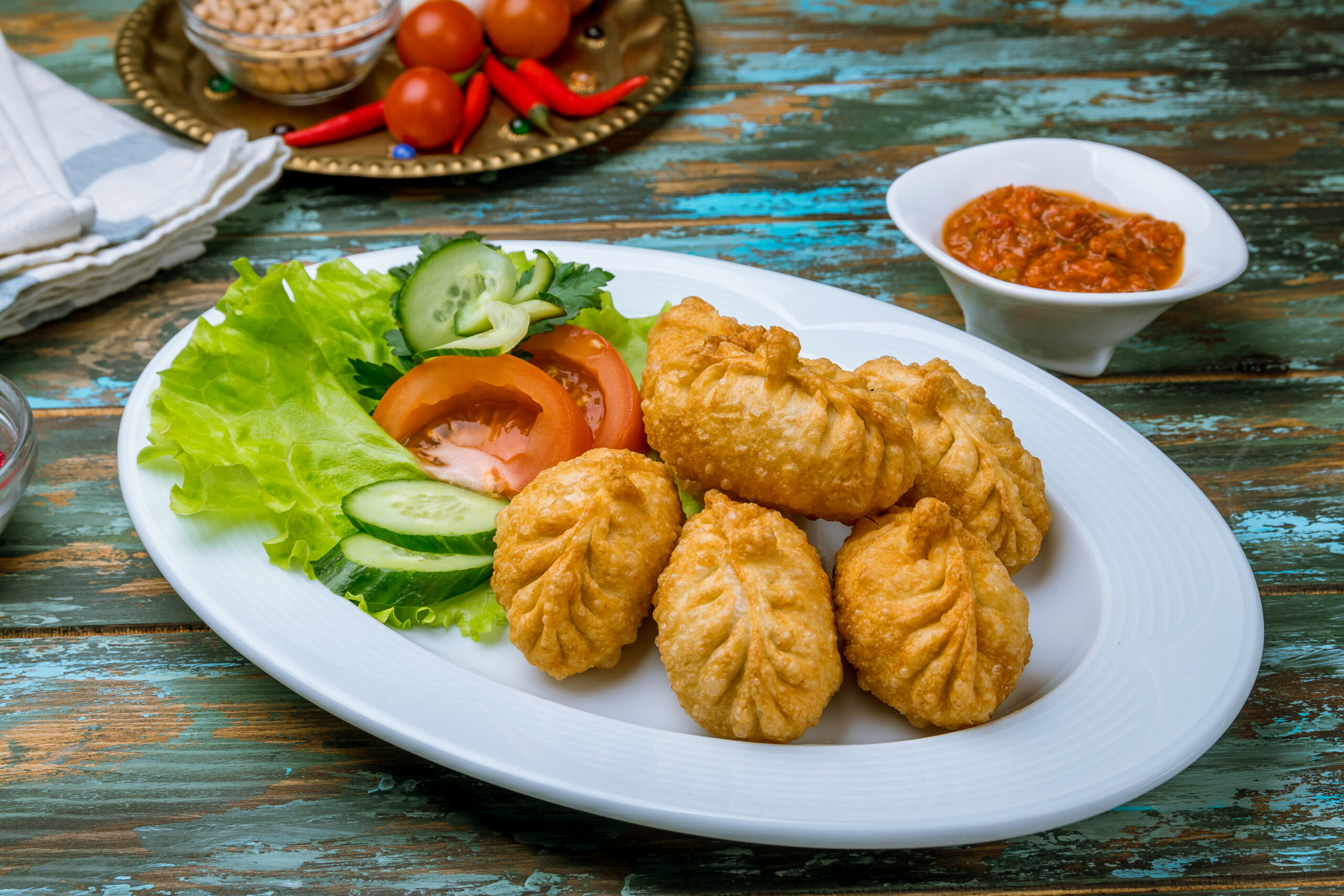 Plate of crispy fried chicken pieces with lettuce, tomato, and cucumber on a white dish, with a dipping sauce on a rustic wooden table.