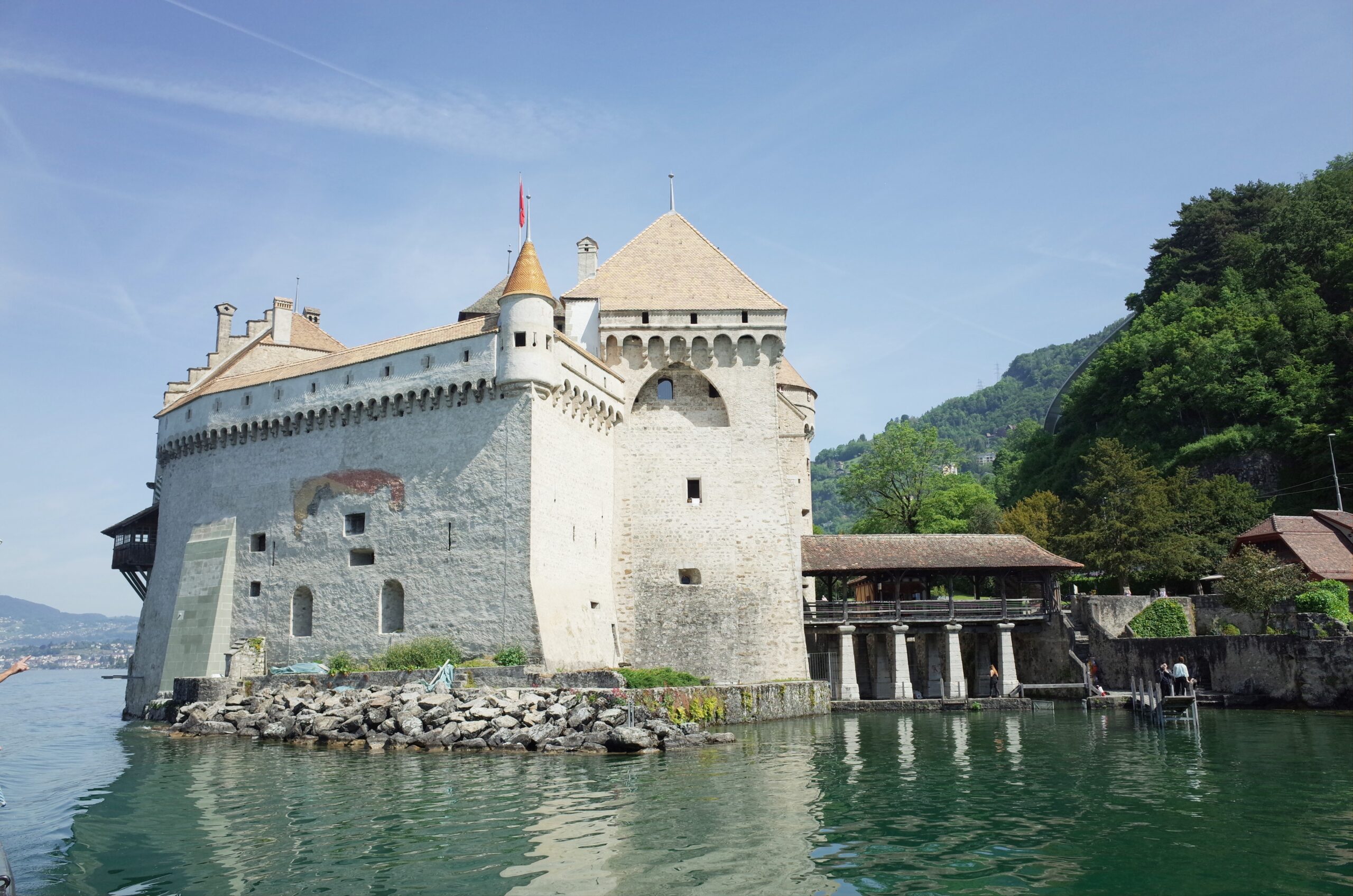 Medieval stone castle by a lake with towers and crenellated walls beneath a clear blue sky.