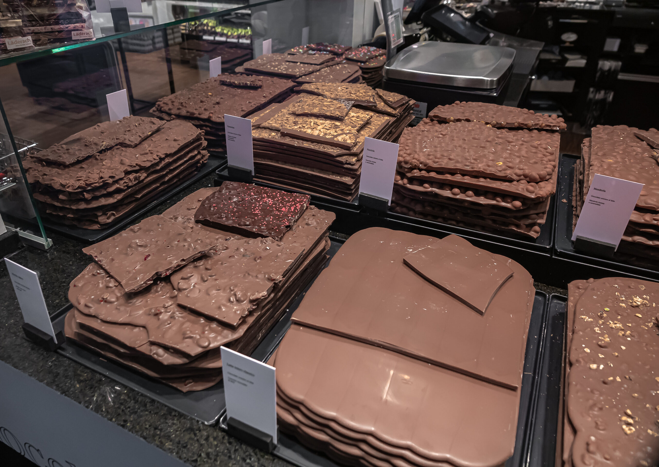 Stacks of large chocolate bars with nuts and sprinkles displayed in a shop case.
