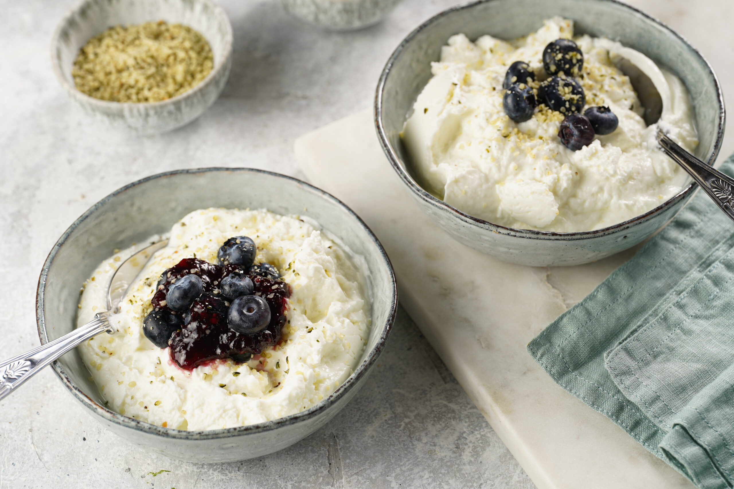 Creamy yogurt dessert with blueberries and crushed nuts in a ceramic bowl, spoon resting in the bowl.