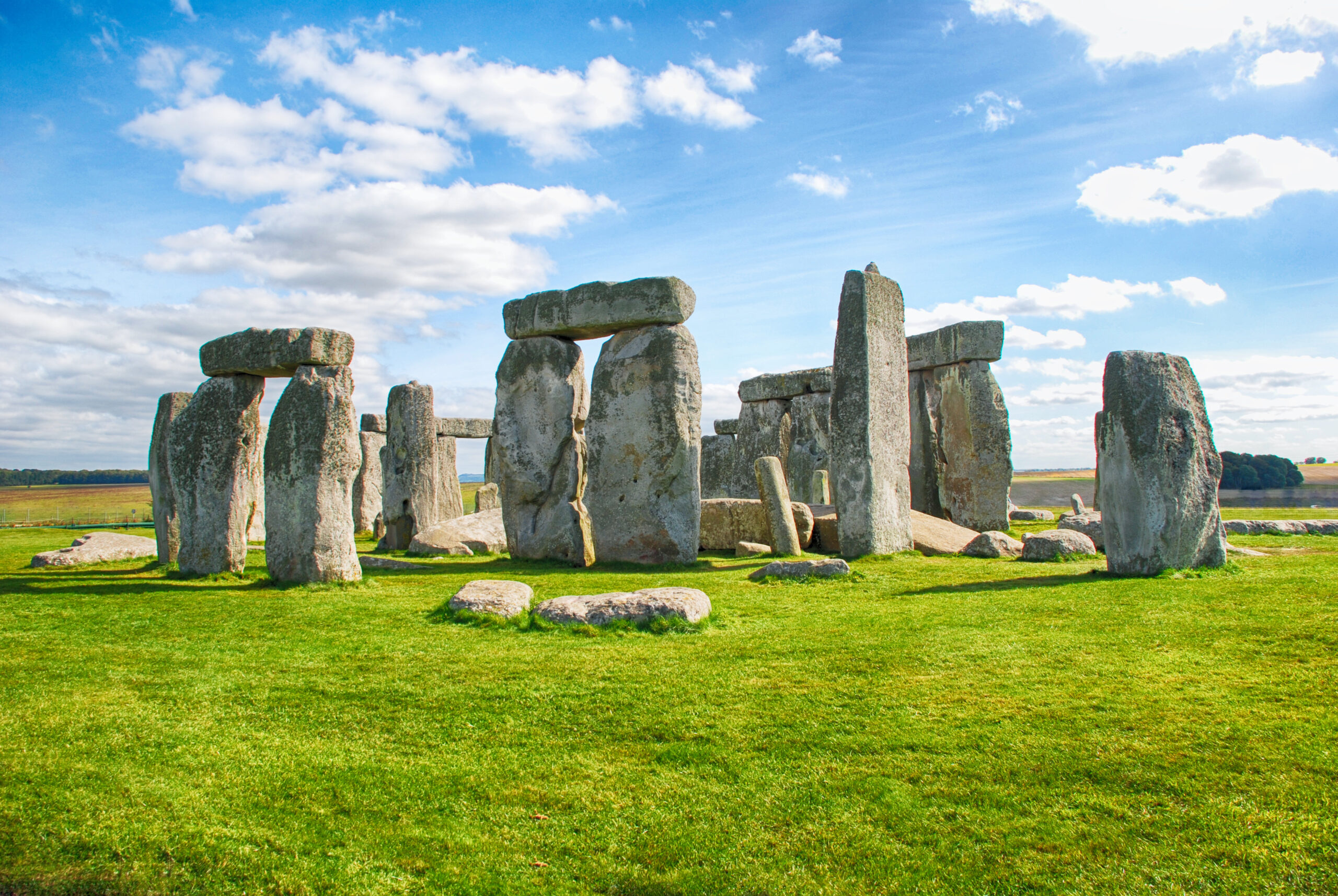 Stone circle of large standing stones in a green field under a blue sky with white clouds.