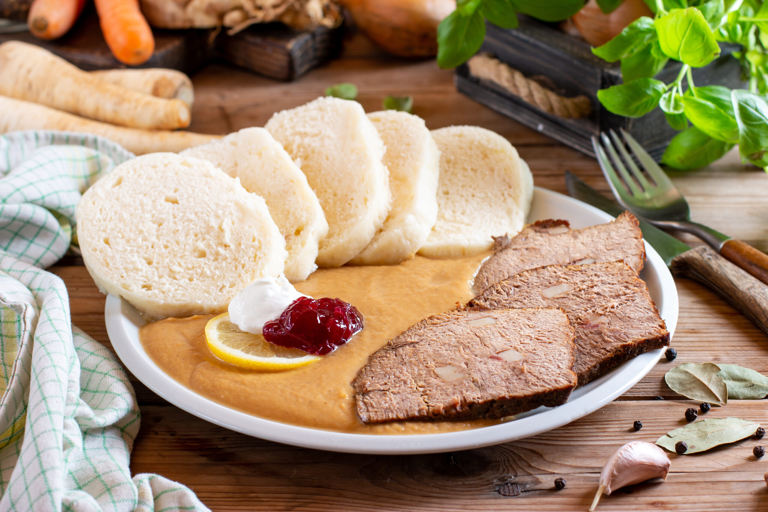Plate with sliced white bread in gravy, thin roast beef slices, lemon wedges, and cranberry sauce on a wooden table