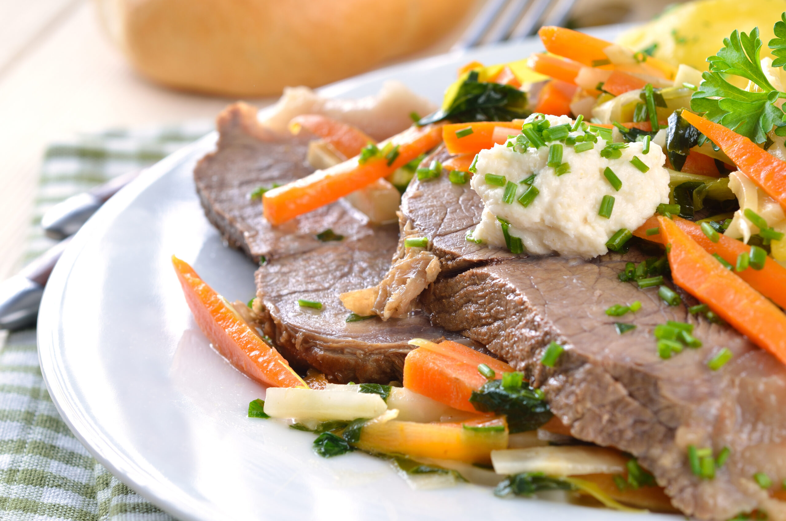 Sliced roast beef with a scoop of mashed potatoes, garnished with chopped chives, and surrounded by carrot sticks and greens on a plate.