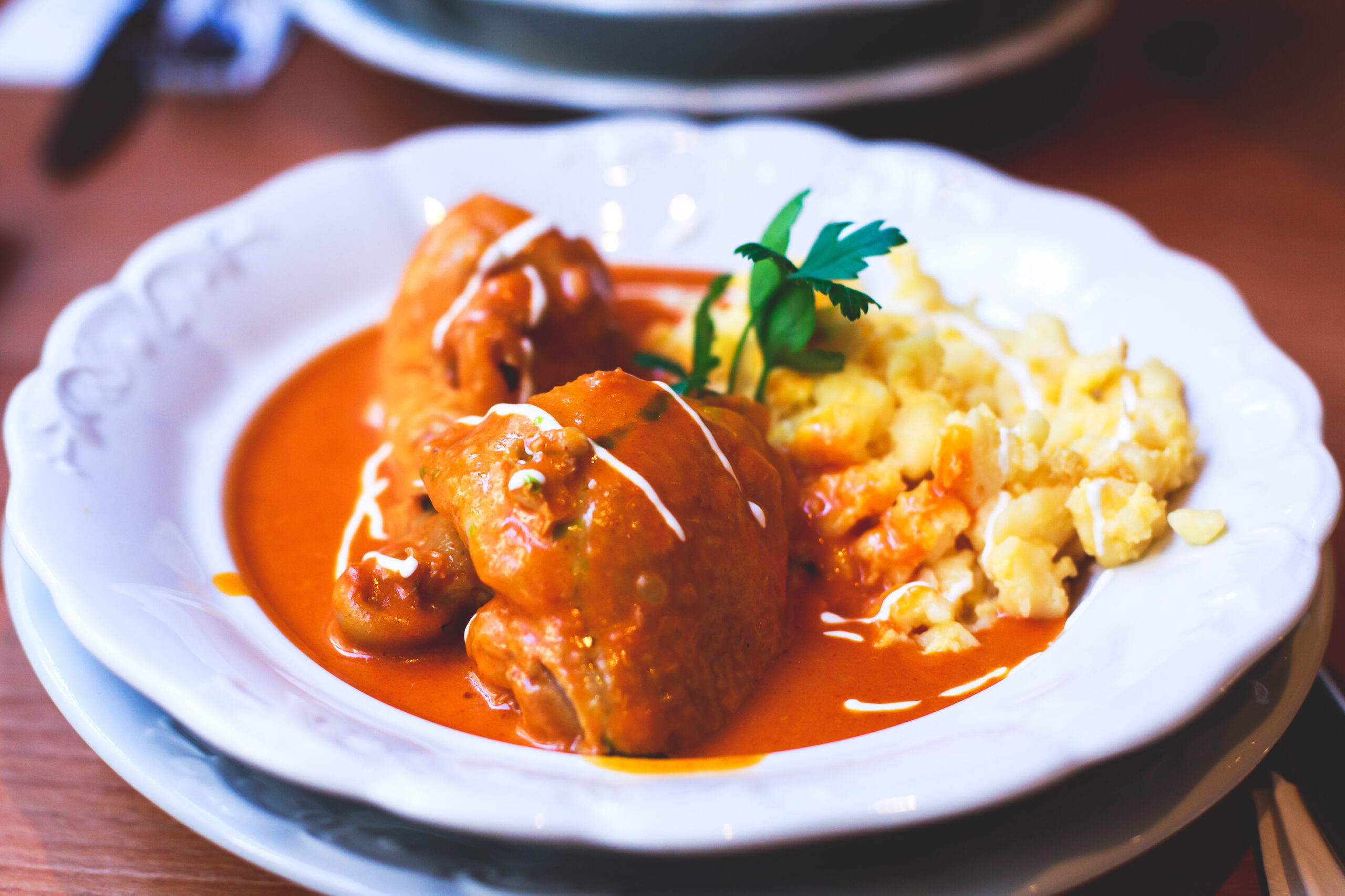 Lobster claws in red sauce on a white plate with mashed potatoes and a parsley garnish, close-up view