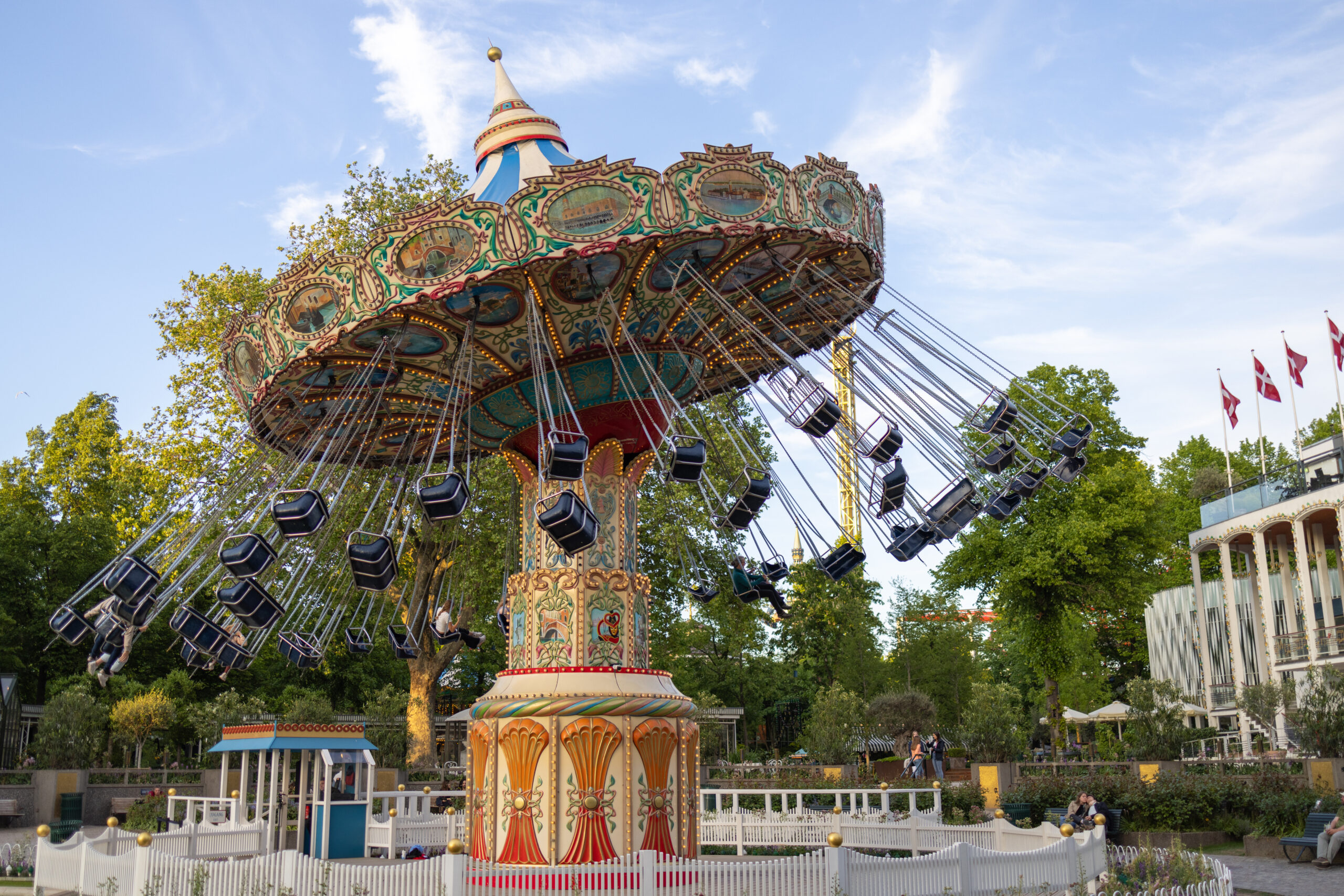 Colorful swing carousel with rotating chairs around an ornate central pillar, set in a park under a blue sky.